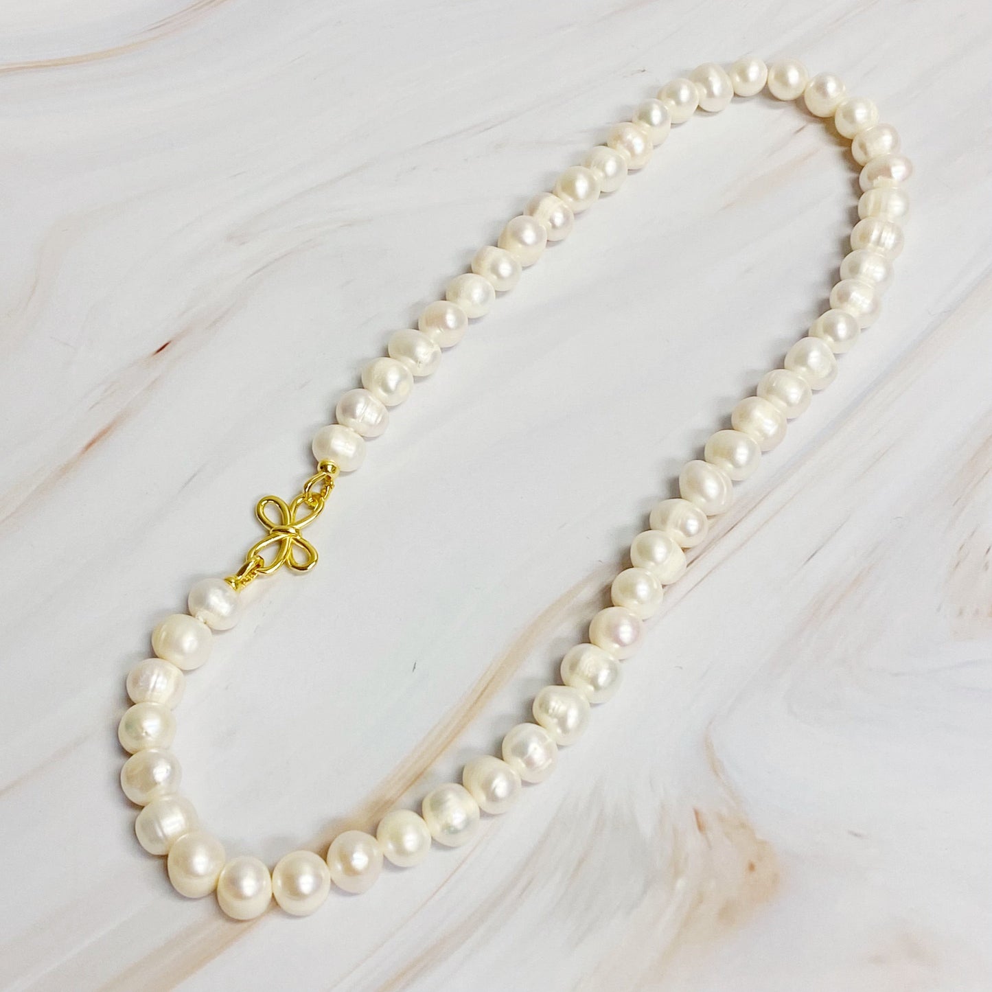 The Clover Clasp Genuine Pearl Necklace by Ellison + Young features rows of round white pearls elegantly displayed on a light surface.