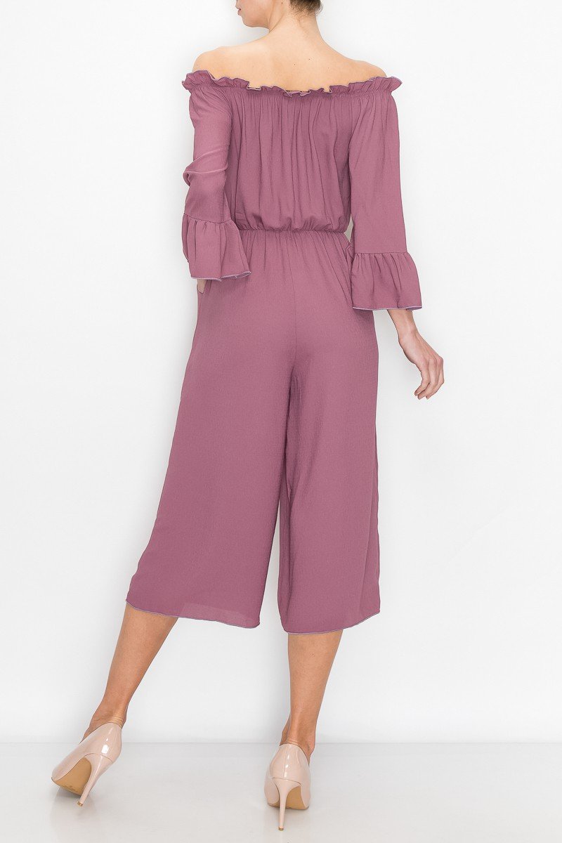 A person in a Stylespect Off Shoulder Jumpsuit - Mauve with bell sleeves and neutral heels poses against a plain white background.