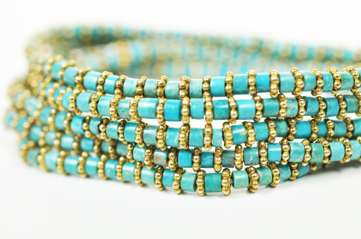 A Gena Myint Turquoise Wrap Bracelet with gold beads is set against a white background.