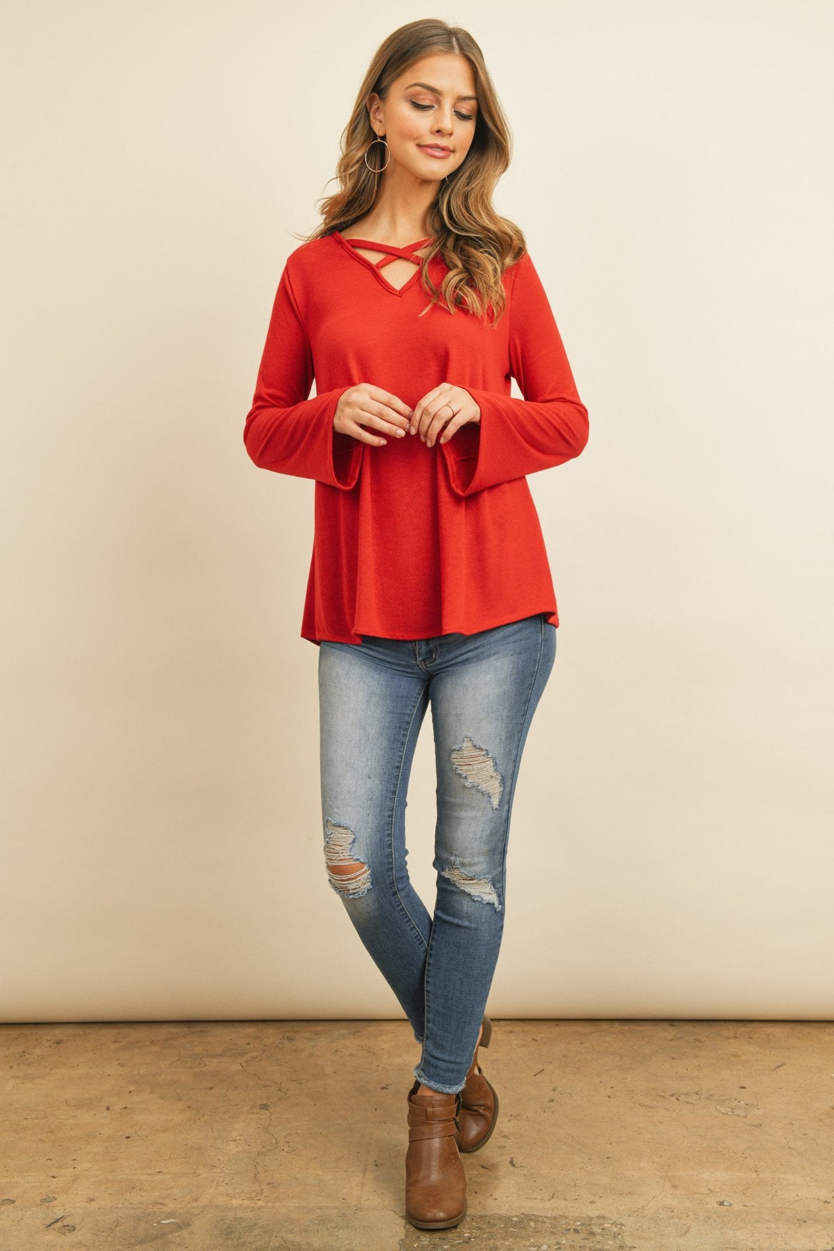 A person wearing a Riah Fashion Criss Cross Neck Long Sleeve Hacci Top in Dusty Blush and blue jeans stands against a neutral background, smiling.
