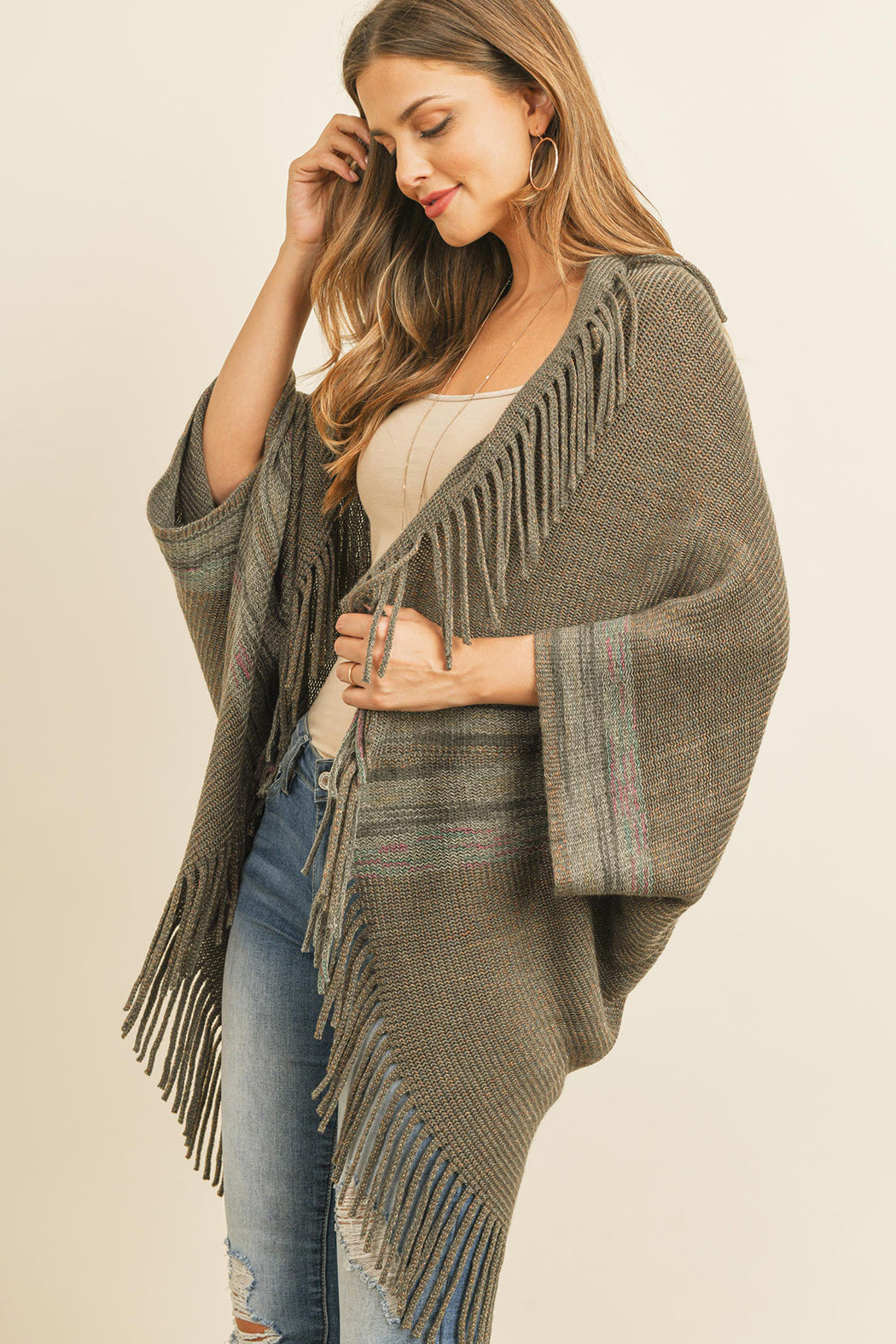 Someone is wearing a Fringe Stripe Open Front Kimono by Riah Fashion over a beige top and ripped jeans, standing against a plain background.
