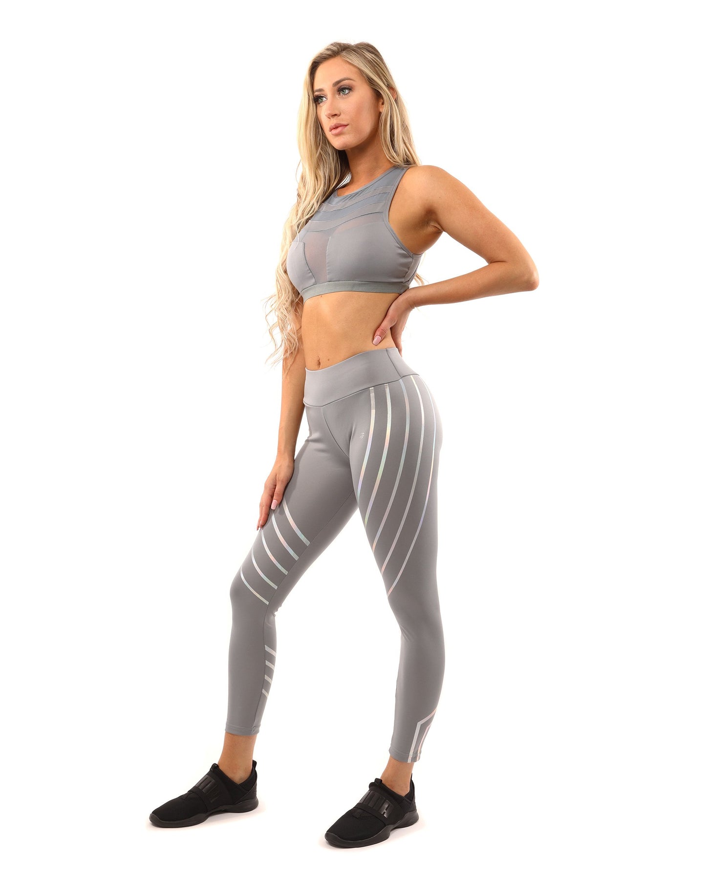 A woman in Savoy Actives grey Laguna Leggings stands on outdoor steps, adjusting her top while facing away from the camera.
