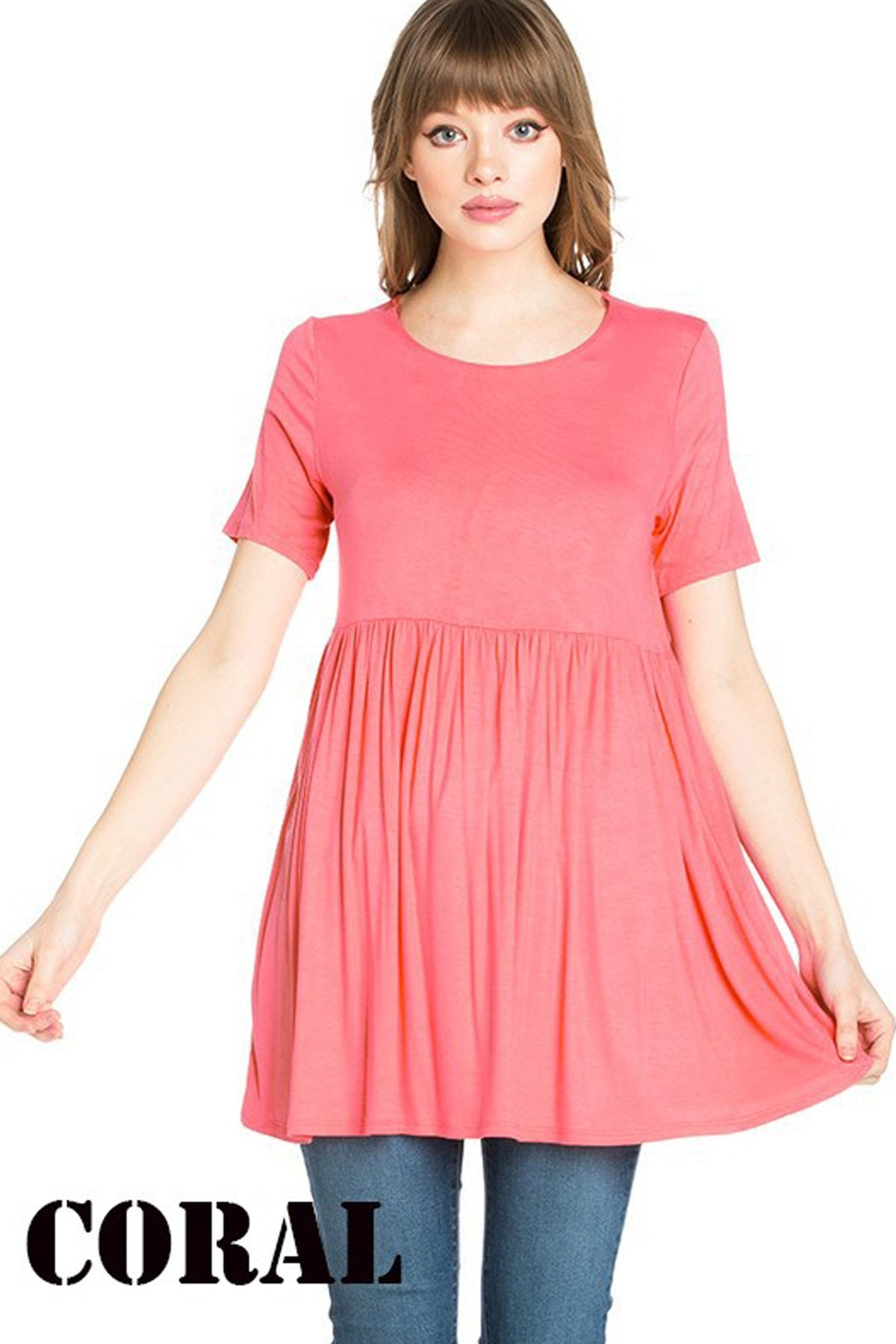 A woman stands outdoors wearing a beige Riah Fashion Short Sleeve Empire Waist Tunic paired with a long necklace.