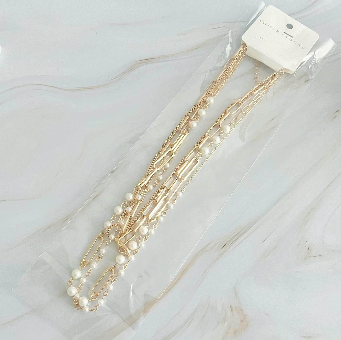 The Fourfect Layered Clip Chain Necklace by Ellison + Young displayed on a white marble surface.