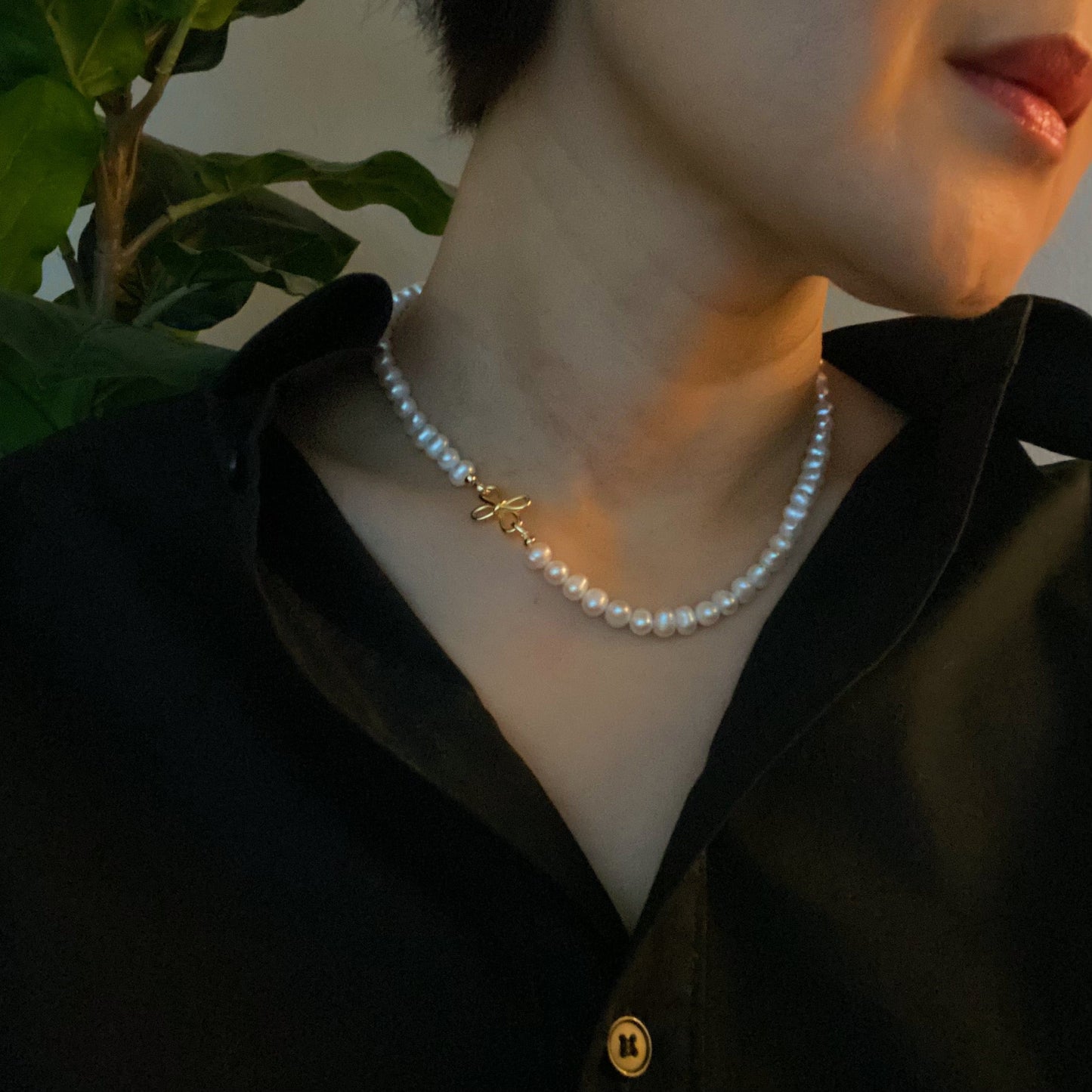 The Clover Clasp Genuine Pearl Necklace by Ellison + Young features rows of round white pearls elegantly displayed on a light surface.