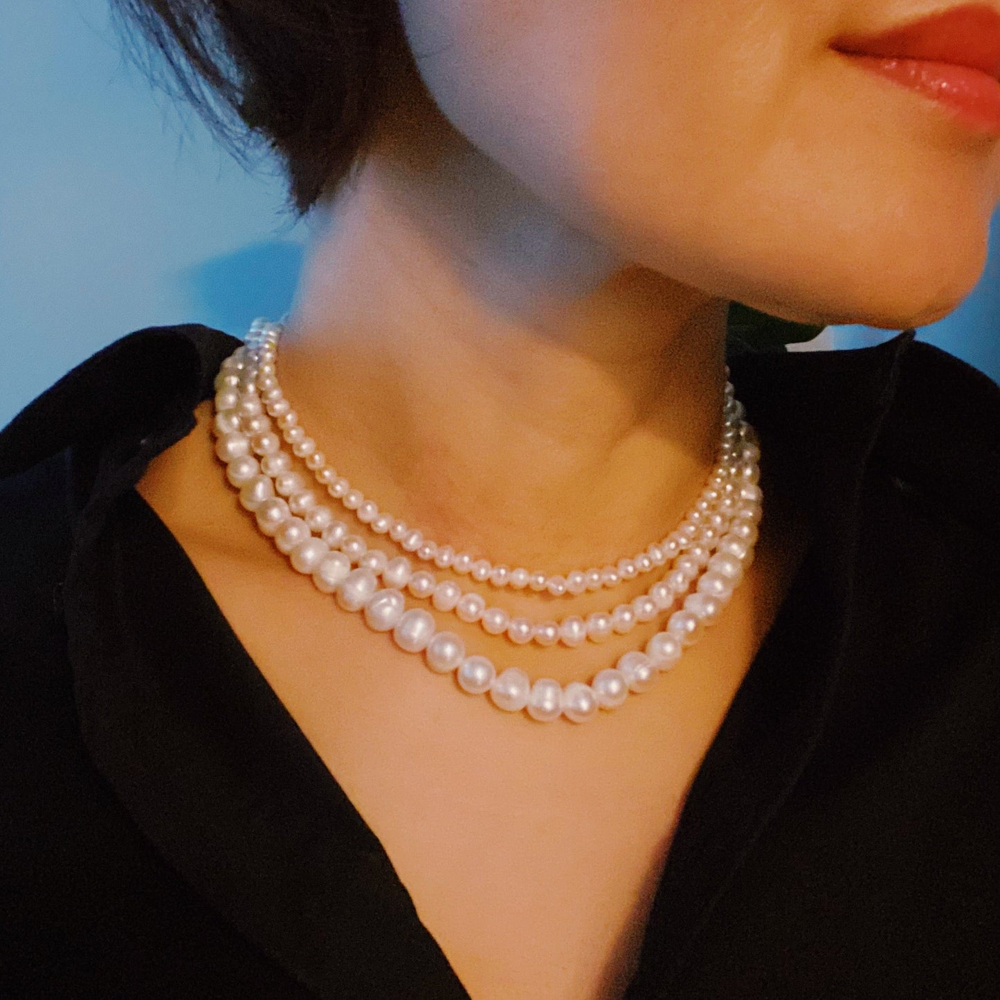 The Clover Clasp Genuine Pearl Necklace by Ellison + Young features rows of round white pearls elegantly displayed on a light surface.