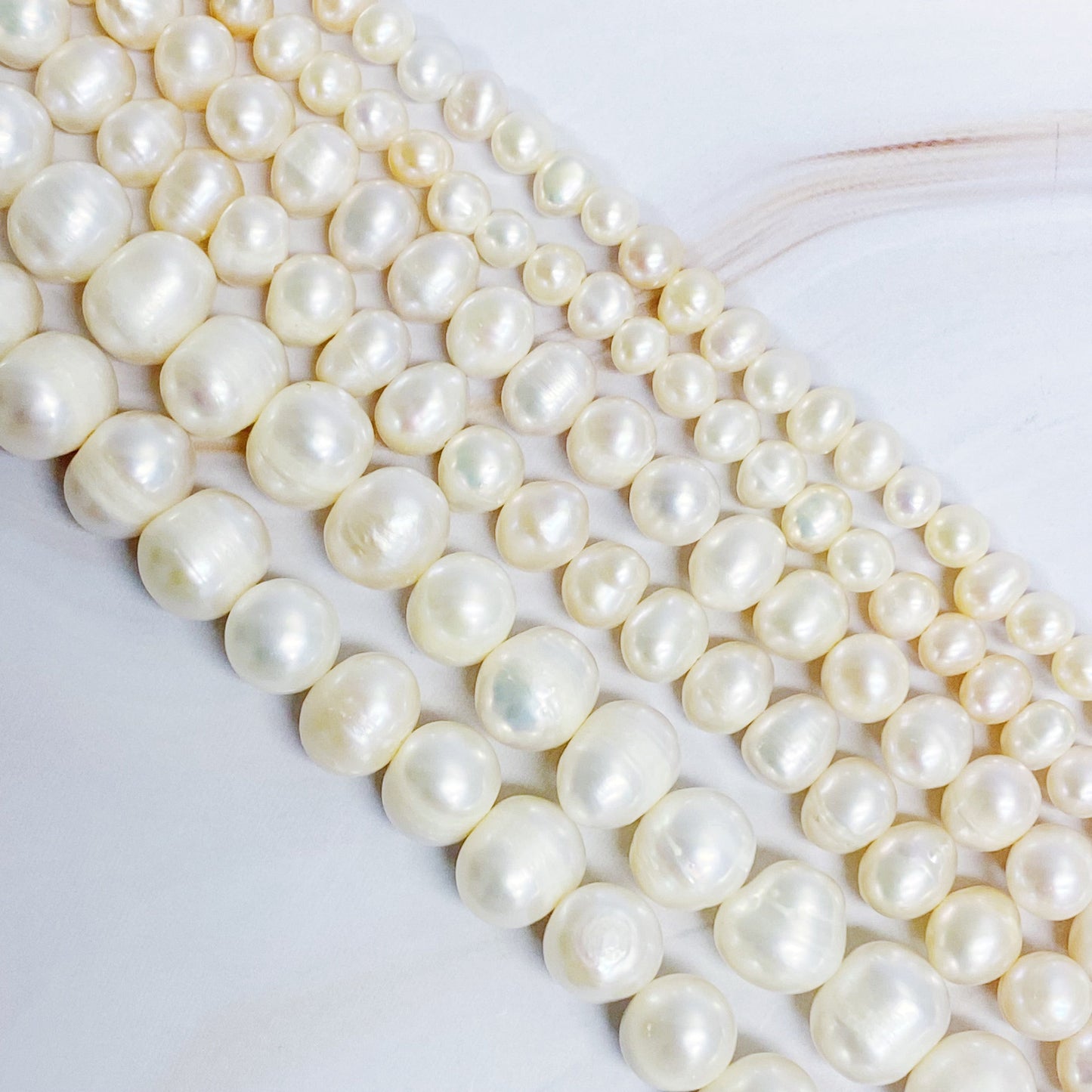 The Clover Clasp Genuine Pearl Necklace by Ellison + Young features rows of round white pearls elegantly displayed on a light surface.