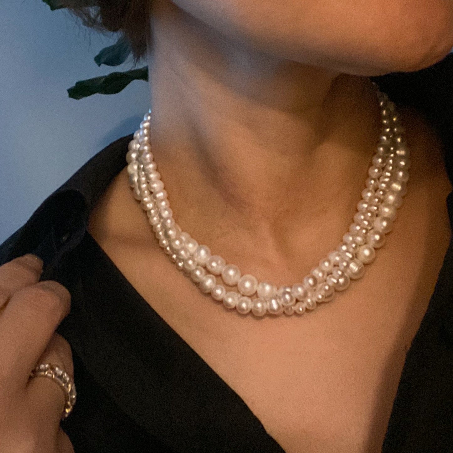 The Clover Clasp Genuine Pearl Necklace by Ellison + Young features rows of round white pearls elegantly displayed on a light surface.