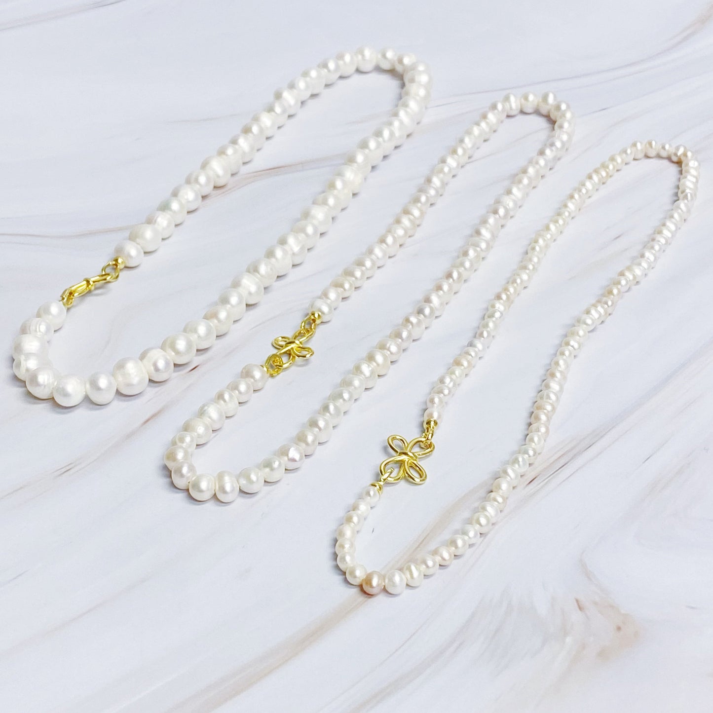 The Clover Clasp Genuine Pearl Necklace by Ellison + Young features rows of round white pearls elegantly displayed on a light surface.