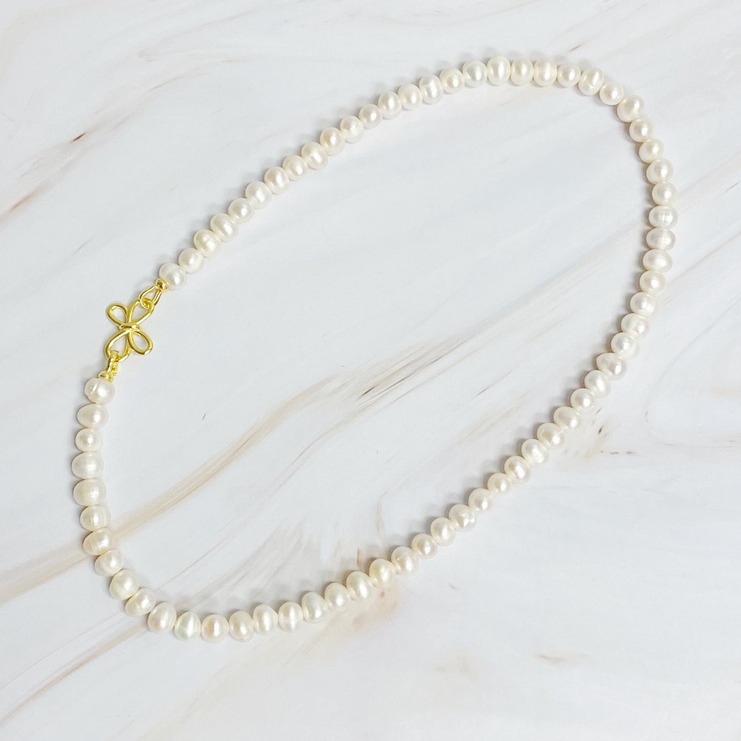 The Clover Clasp Genuine Pearl Necklace by Ellison + Young features rows of round white pearls elegantly displayed on a light surface.