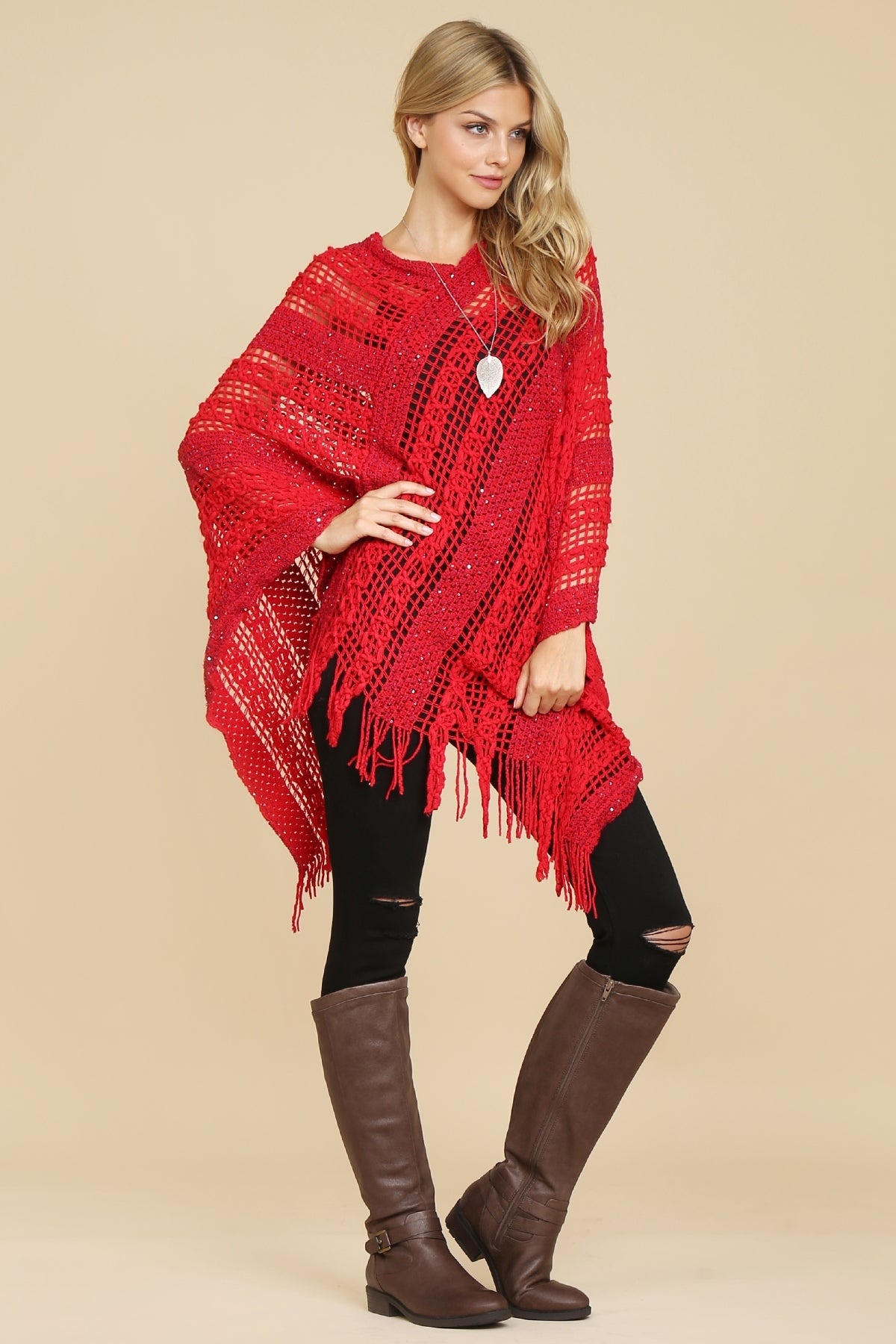 A woman in a Riah Fashion Hdf2097 - Crochet Native Pattern Poncho paired with black pants and brown knee-high boots stands against a neutral background.