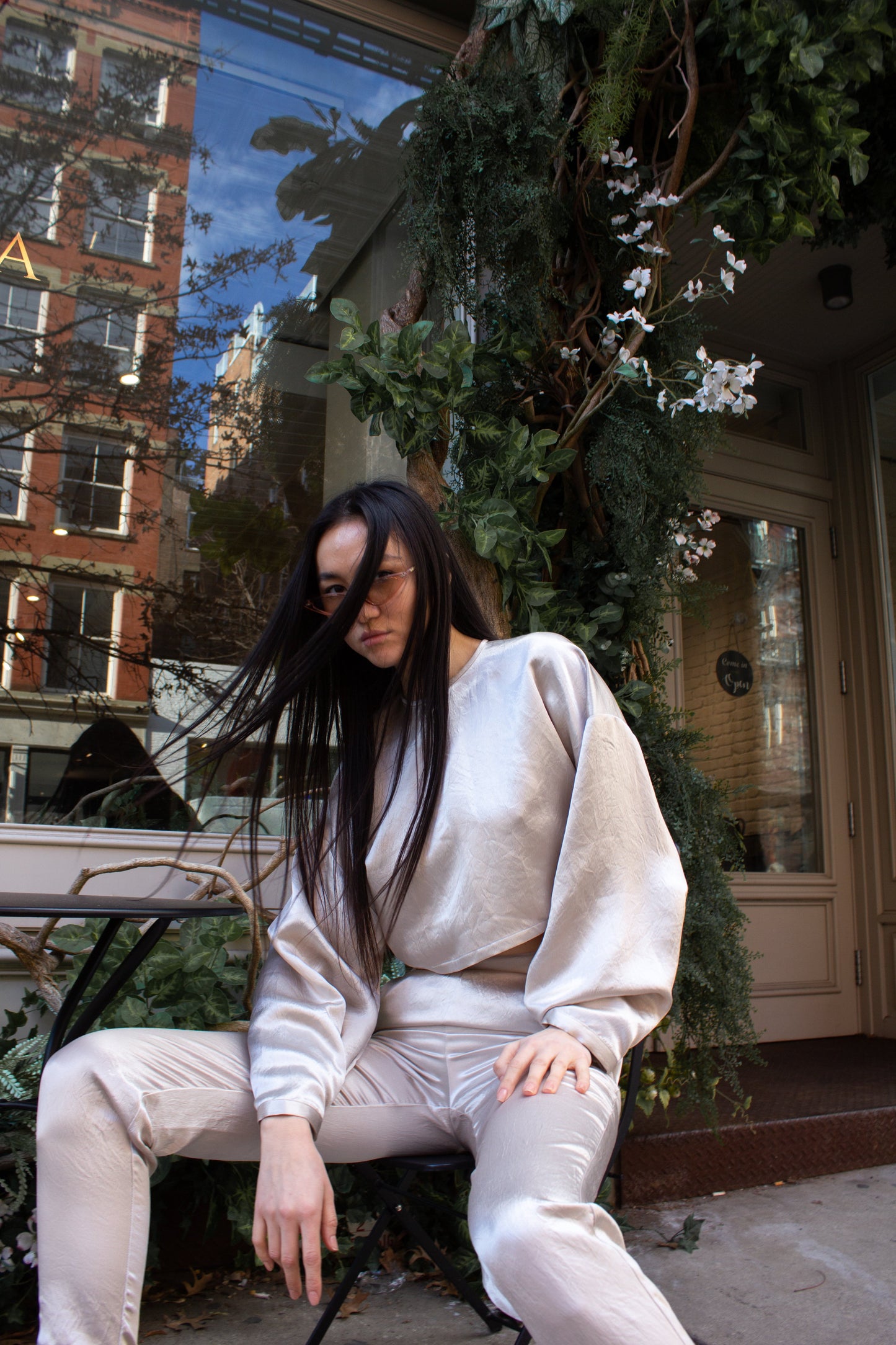 The Sophie Beige Top by Le Réussi® is a shiny, metallic silver long-sleeve crop top featuring a high neckline and loose fit, displayed on a white background.