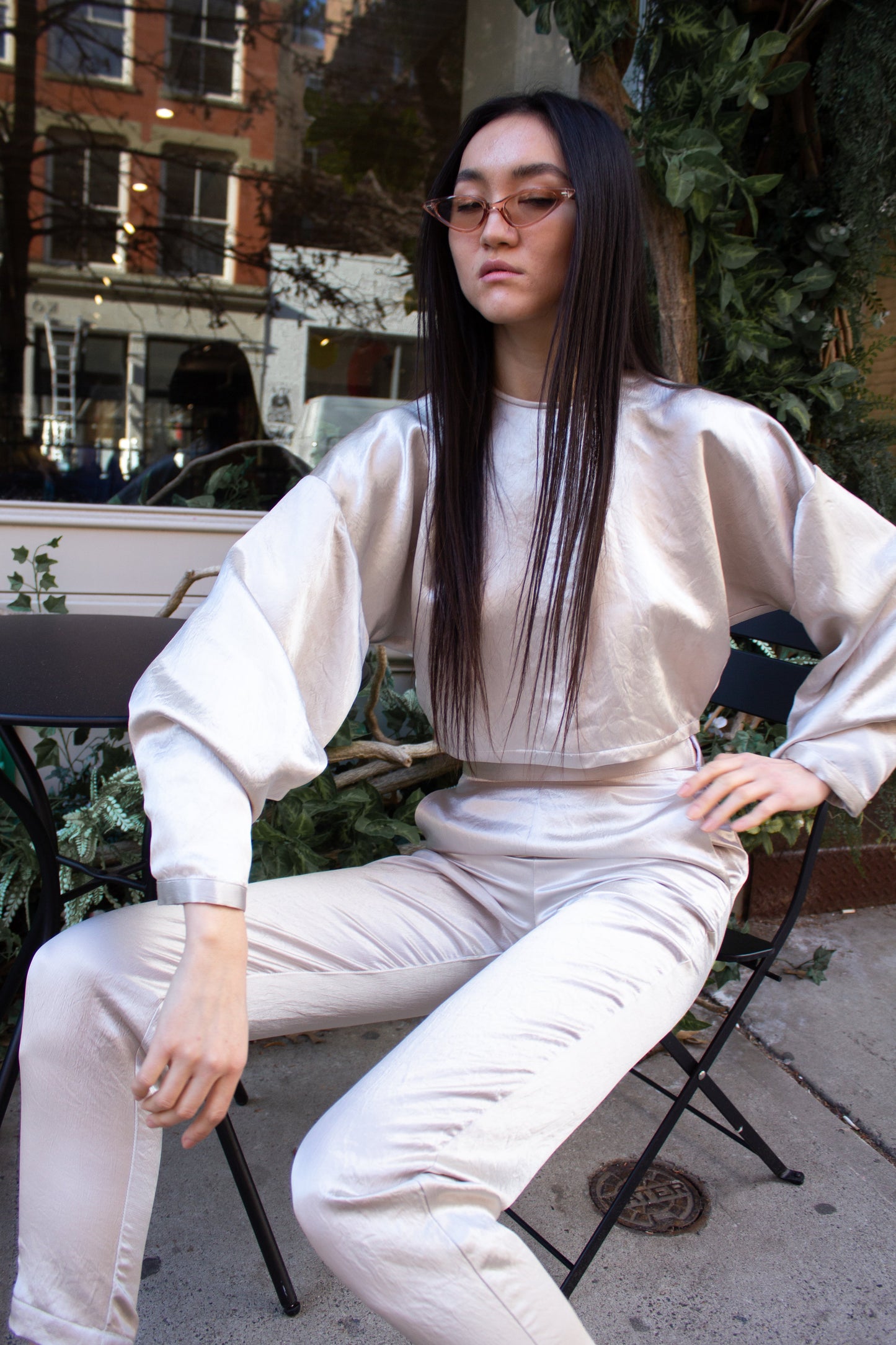 The Sophie Beige Top by Le Réussi® is a shiny, metallic silver long-sleeve crop top featuring a high neckline and loose fit, displayed on a white background.