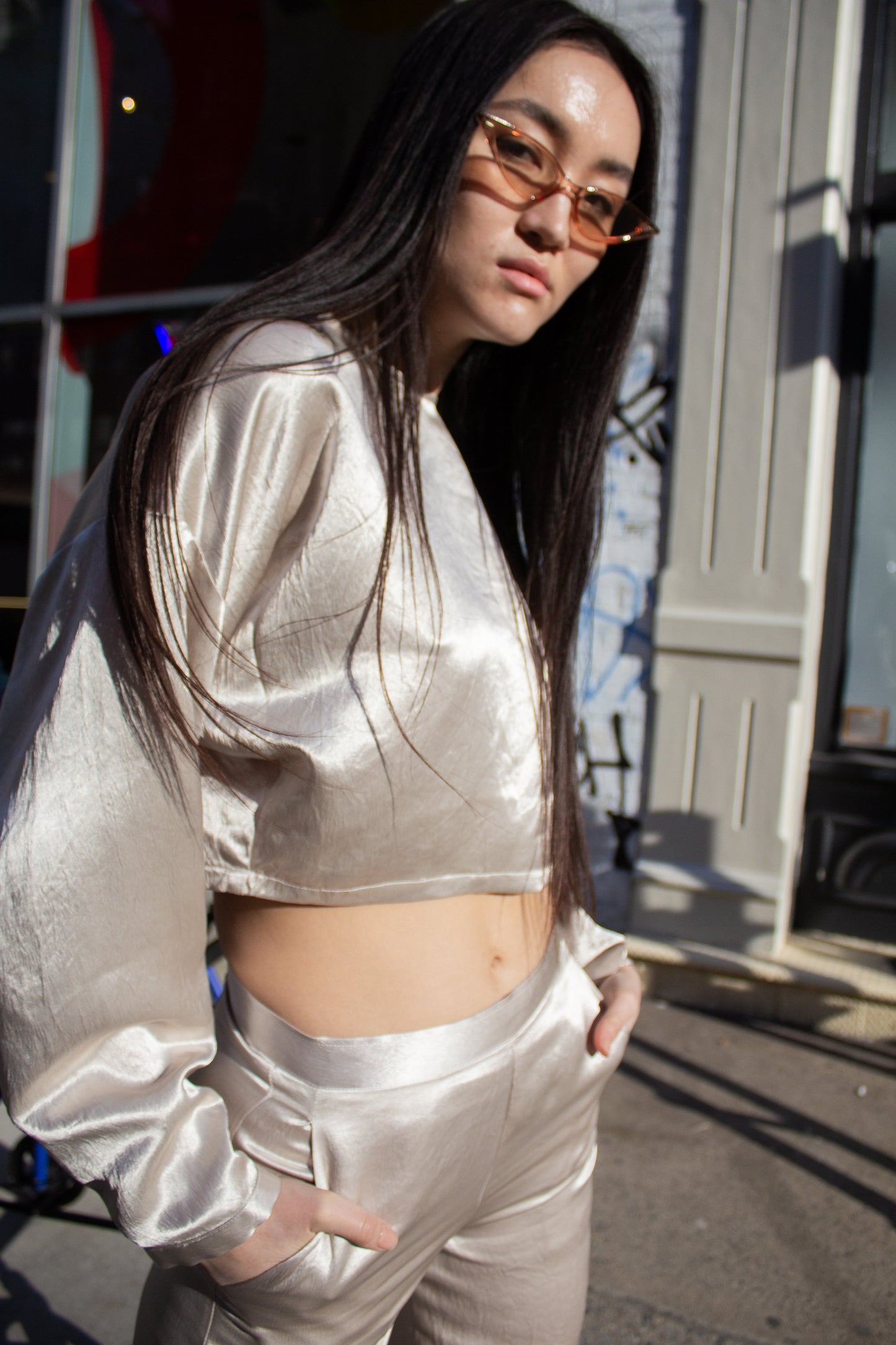 The Sophie Beige Top by Le Réussi® is a shiny, metallic silver long-sleeve crop top featuring a high neckline and loose fit, displayed on a white background.