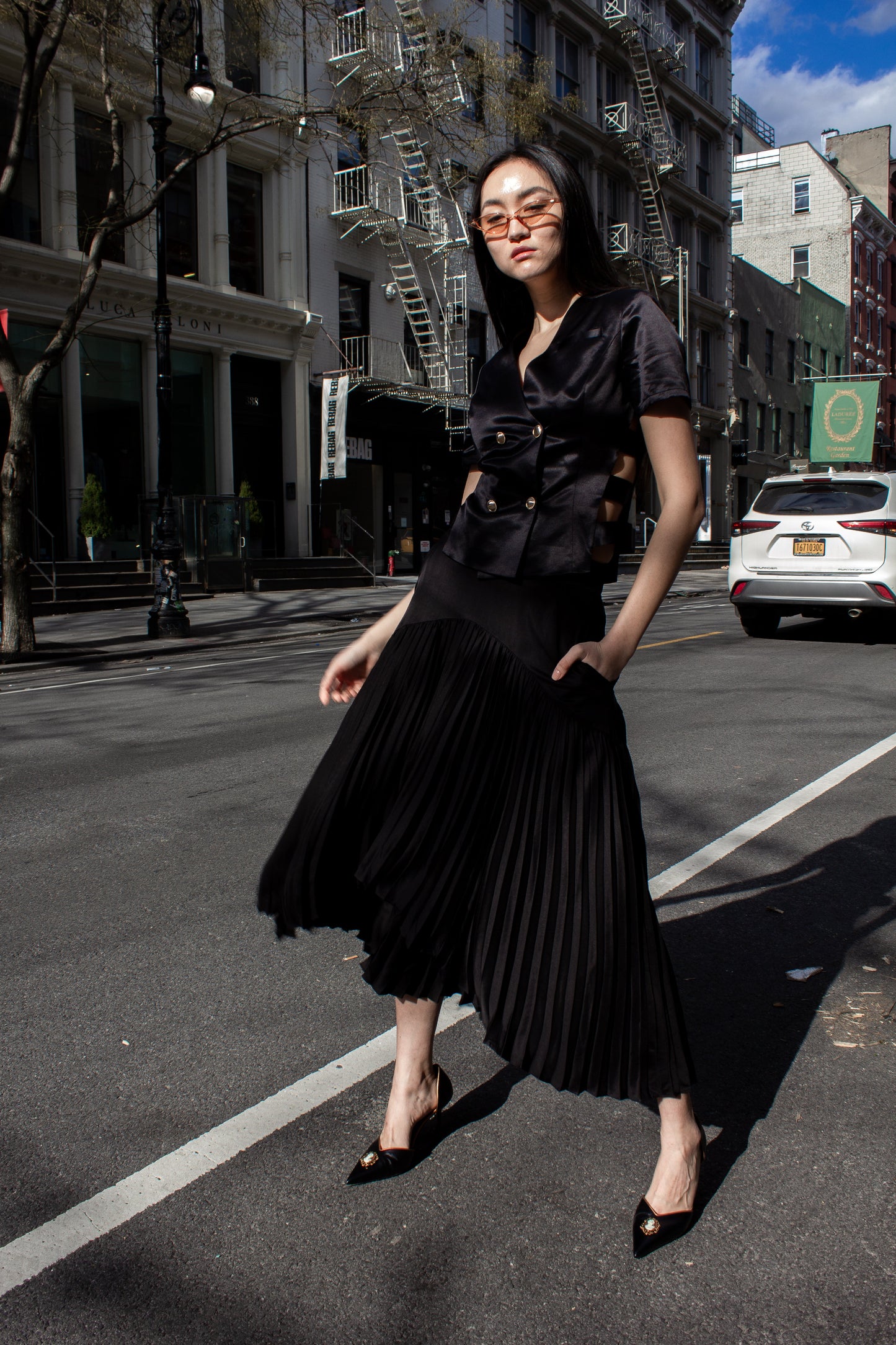 The Maryanne Black Skirt by Le Réussi® features a high-low hemline with pleats and a smooth fabric at the waist and upper section.