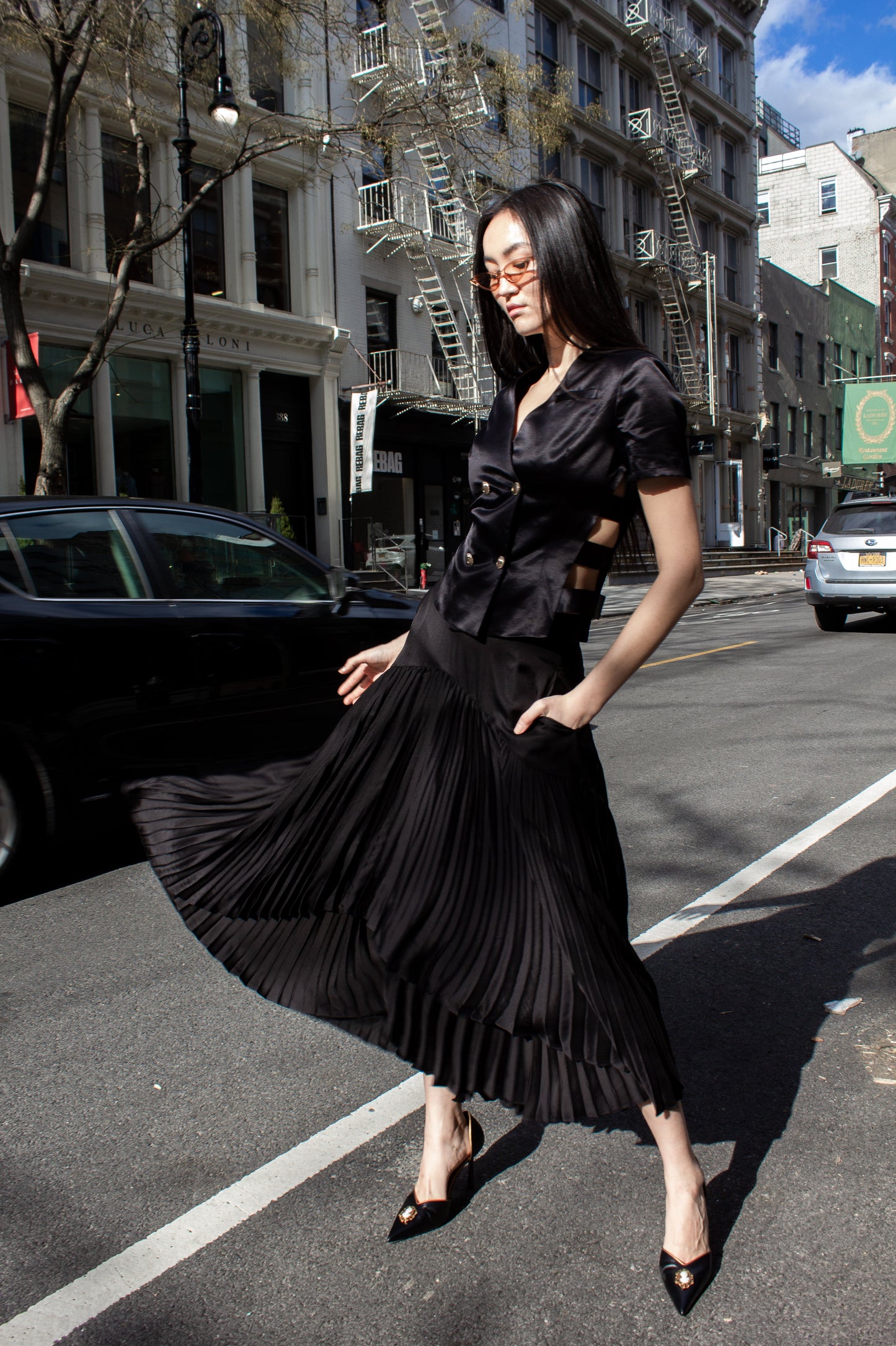 The Maryanne Black Skirt by Le Réussi® features a high-low hemline with pleats and a smooth fabric at the waist and upper section.