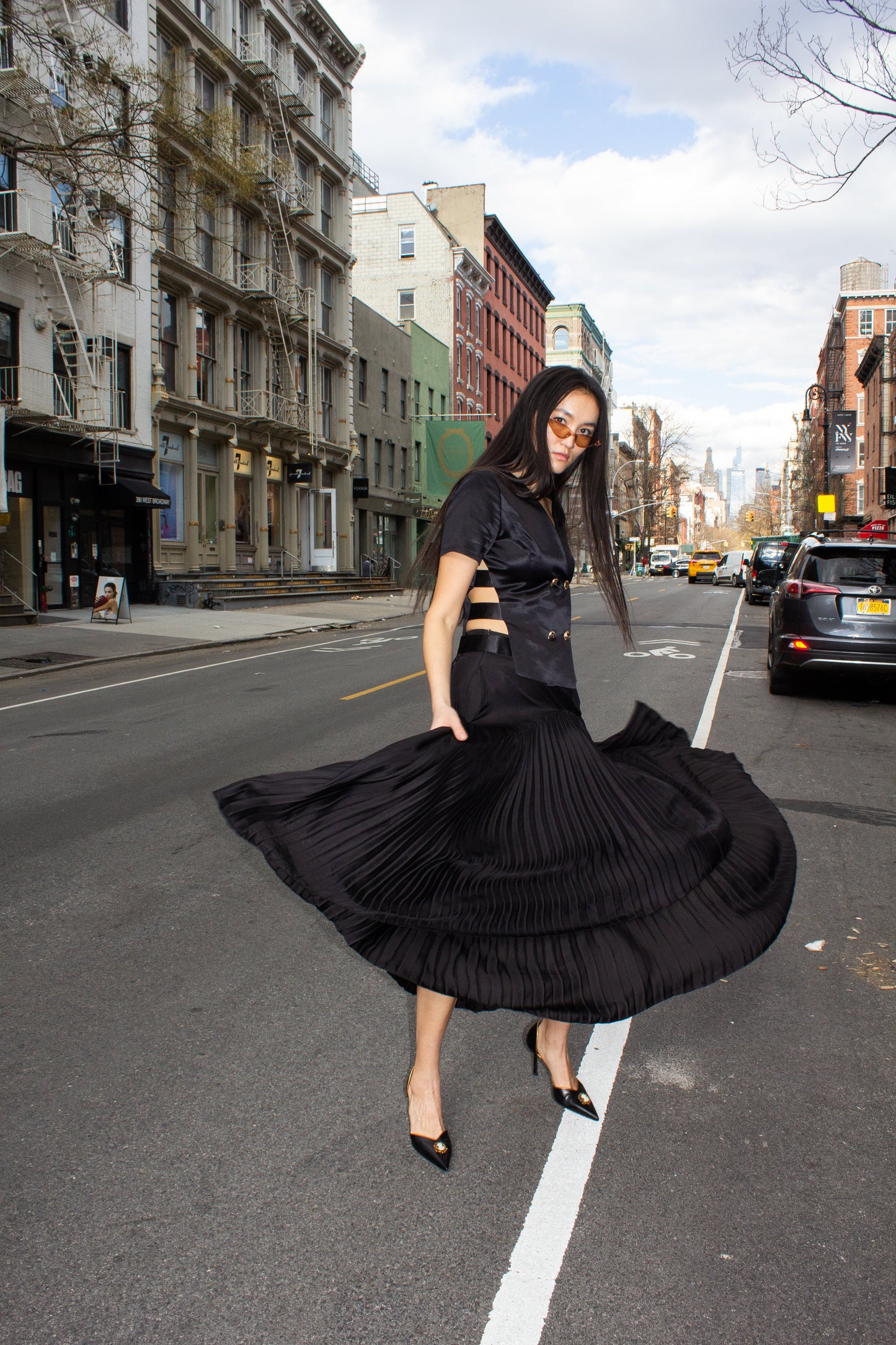 The Maryanne Black Skirt by Le Réussi® features a high-low hemline with pleats and a smooth fabric at the waist and upper section.