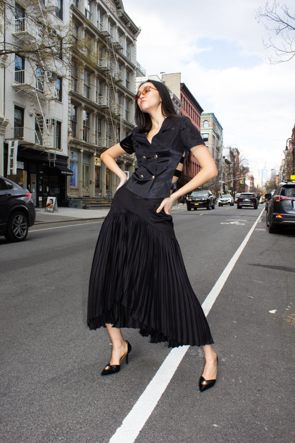 The Maryanne Black Skirt by Le Réussi® features a high-low hemline with pleats and a smooth fabric at the waist and upper section.