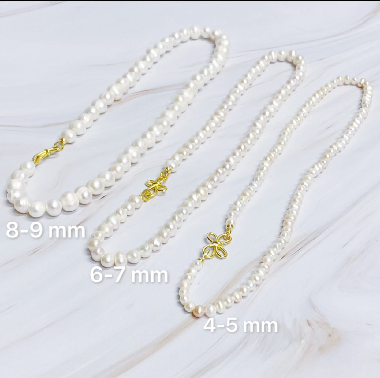 The Clover Clasp Genuine Pearl Necklace by Ellison + Young features rows of round white pearls elegantly displayed on a light surface.