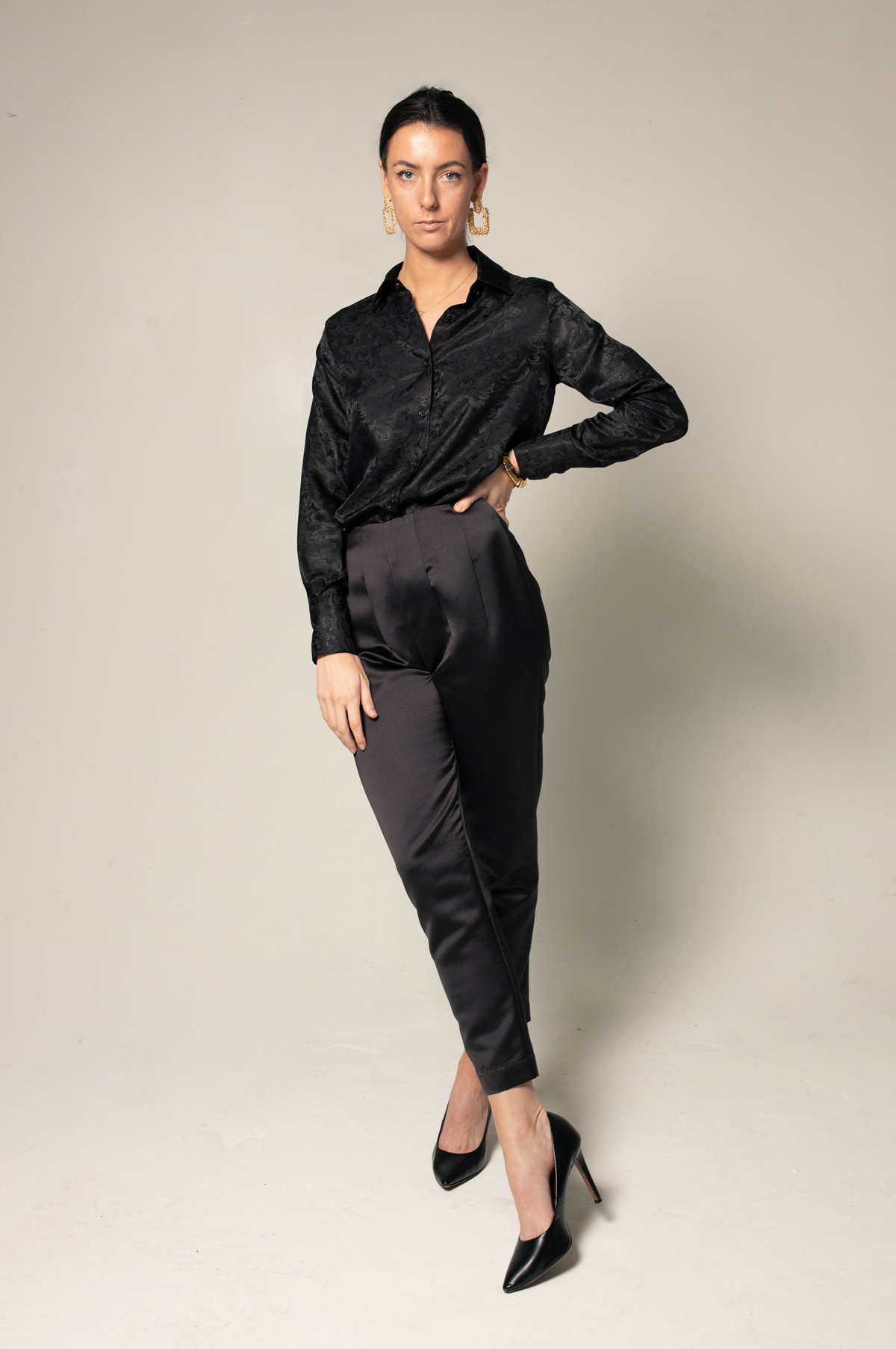 Someone wearing Le Réussi® Womens Trousers Pleated Pants and a black shirt stands against a plain background with one hand on their hip.