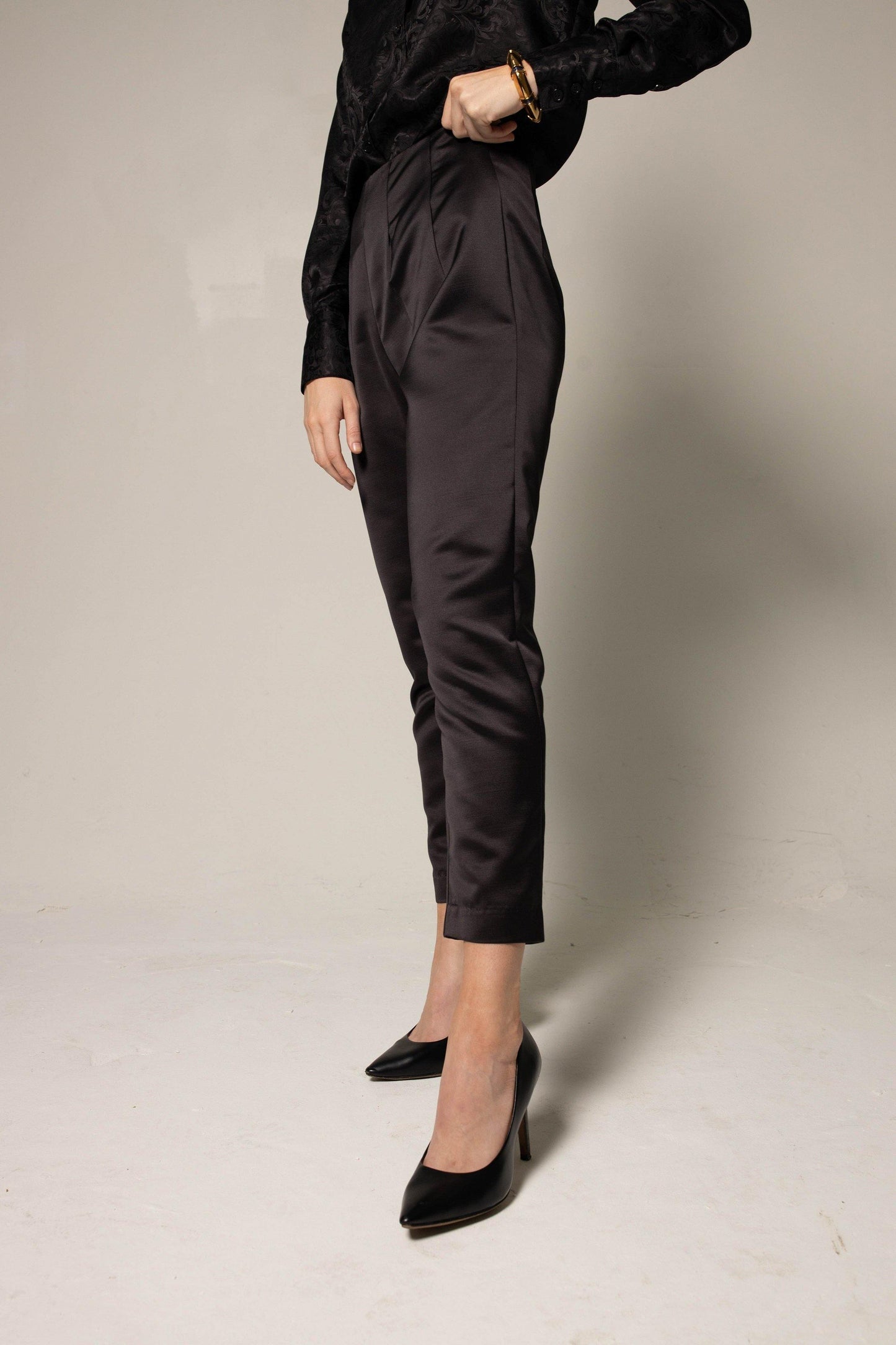 Someone wearing Le Réussi® Womens Trousers Pleated Pants and a black shirt stands against a plain background with one hand on their hip.