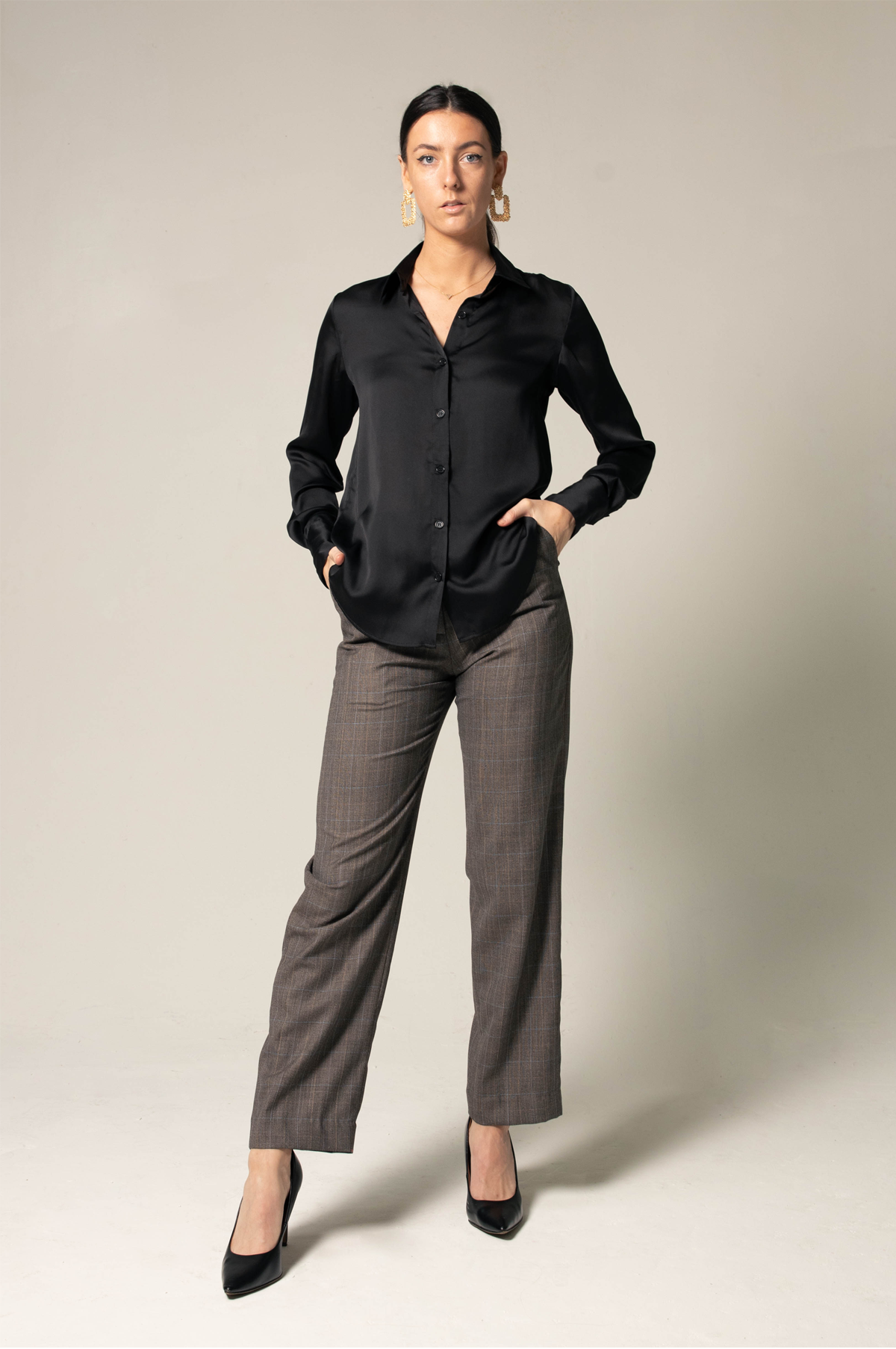 A person in a black shirt and Le Réussi® Womens Straight Leg Pants stands confidently with hands in pockets, wearing black heels against a neutral background.