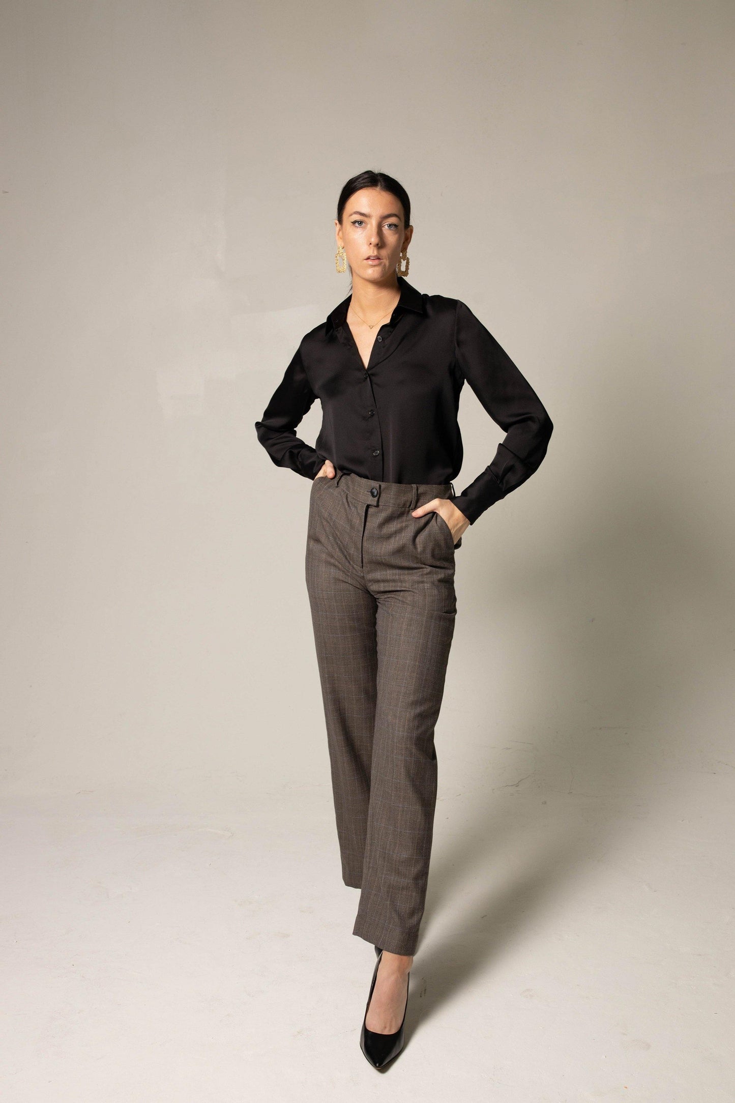 A person in a black shirt and Le Réussi® Womens Straight Leg Pants stands confidently with hands in pockets, wearing black heels against a neutral background.