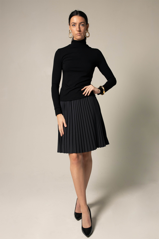 Sporting a black turtleneck, Le Réussi® Classy Pleated Skirt, and heels, a person stands in a side pose against a plain background.