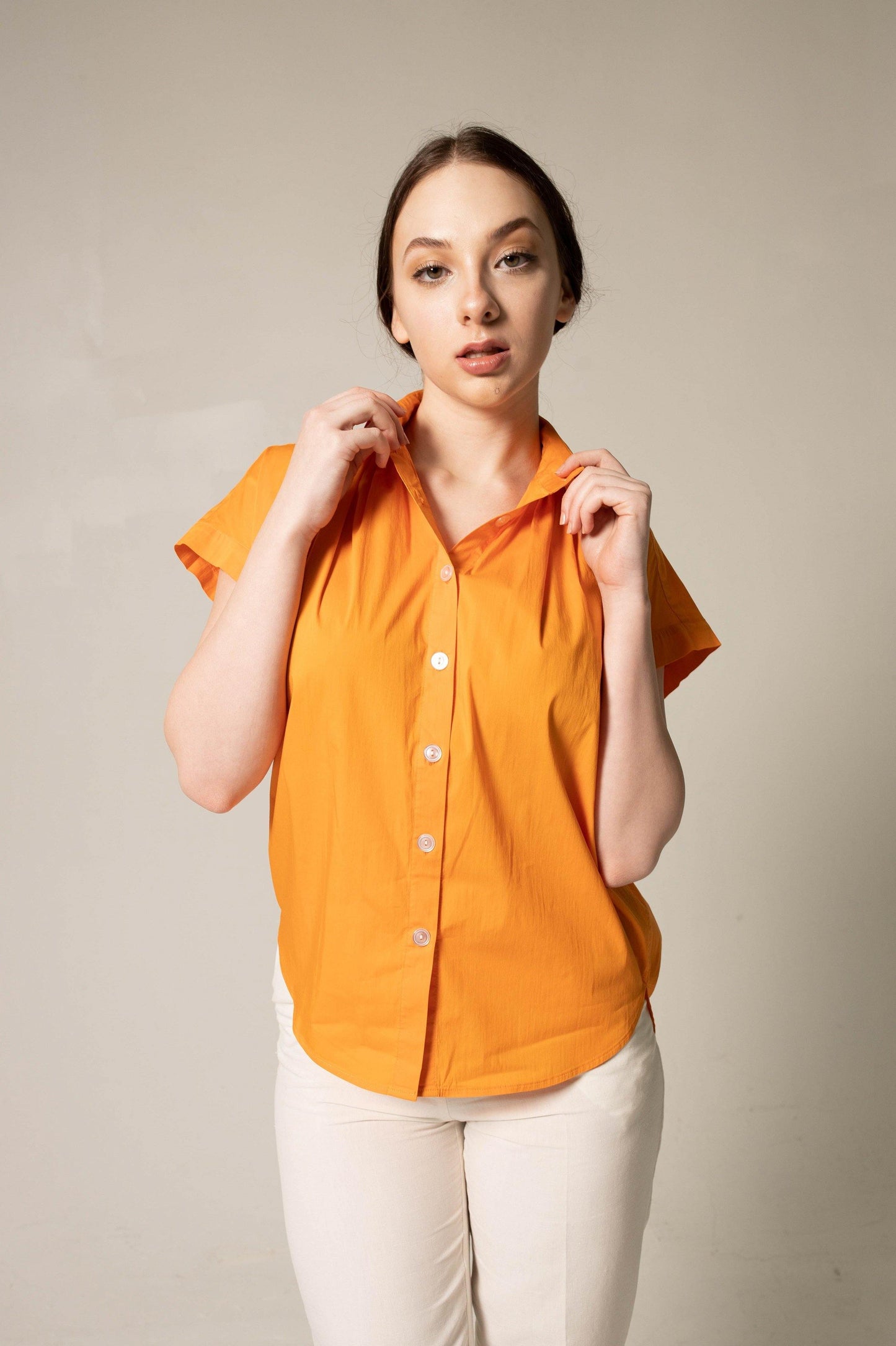 A person poses against a plain background, wearing the Womens Gather Collar Shirt in Orange by Le Réussi® and white pants.