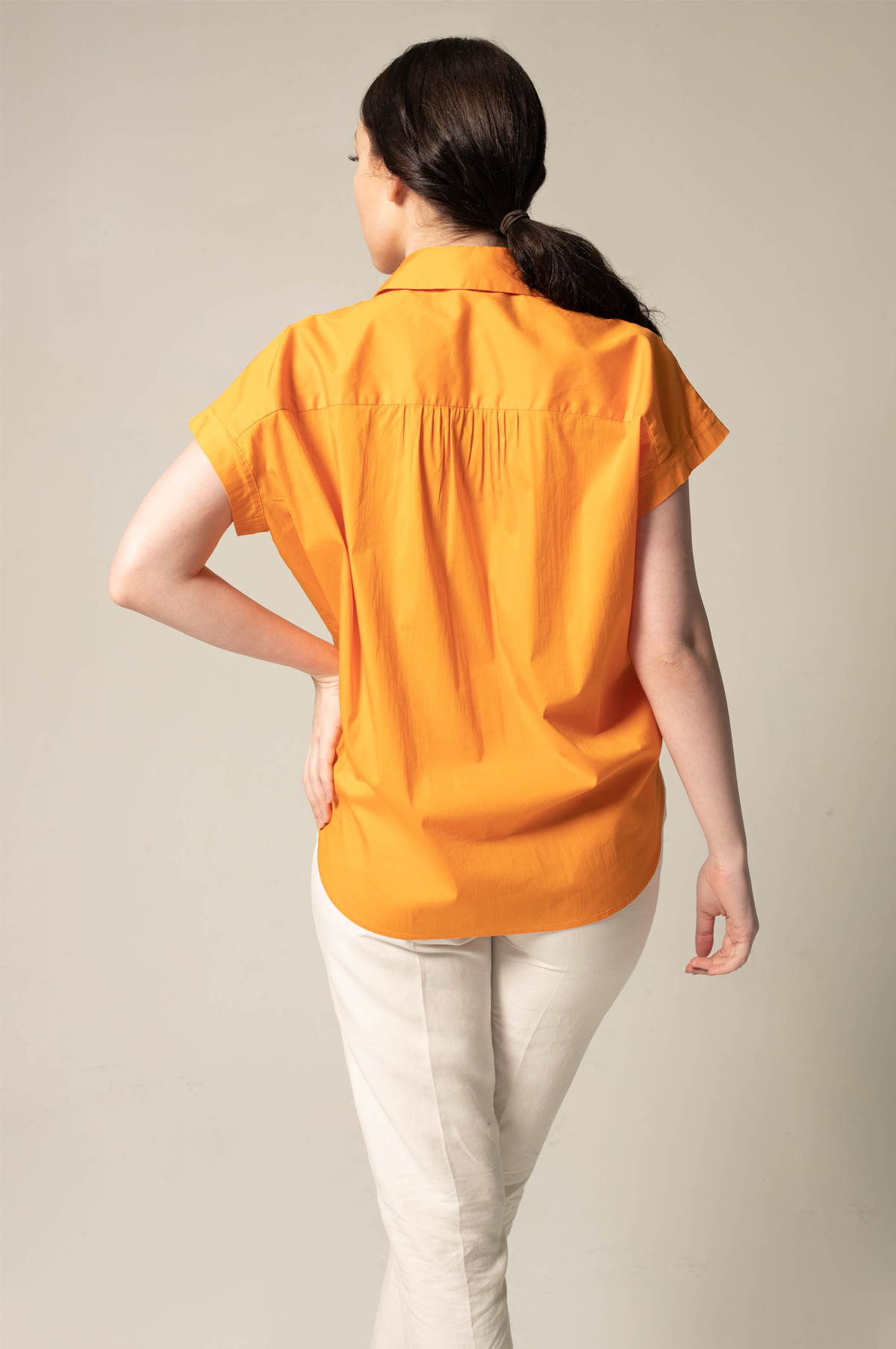 A person poses against a plain background, wearing the Womens Gather Collar Shirt in Orange by Le Réussi® and white pants.