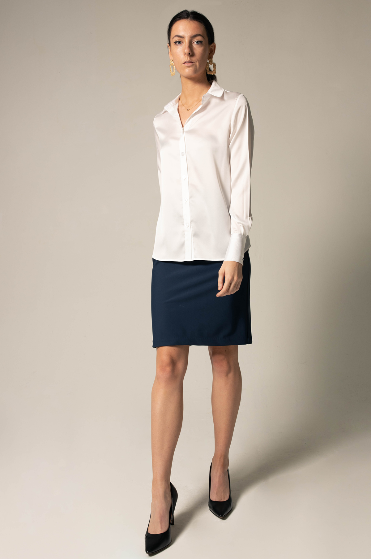 A woman poses against a neutral background wearing the Elegance Silk Shirt in White by Le Réussi®, paired with a dark skirt.