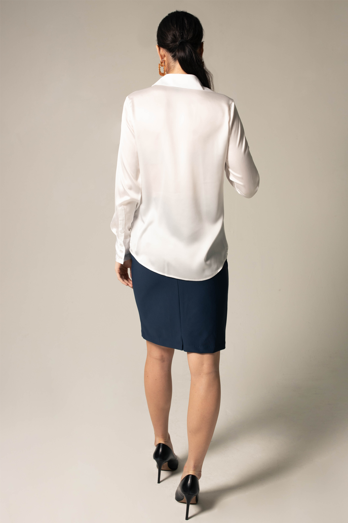 A woman poses against a neutral background wearing the Elegance Silk Shirt in White by Le Réussi®, paired with a dark skirt.
