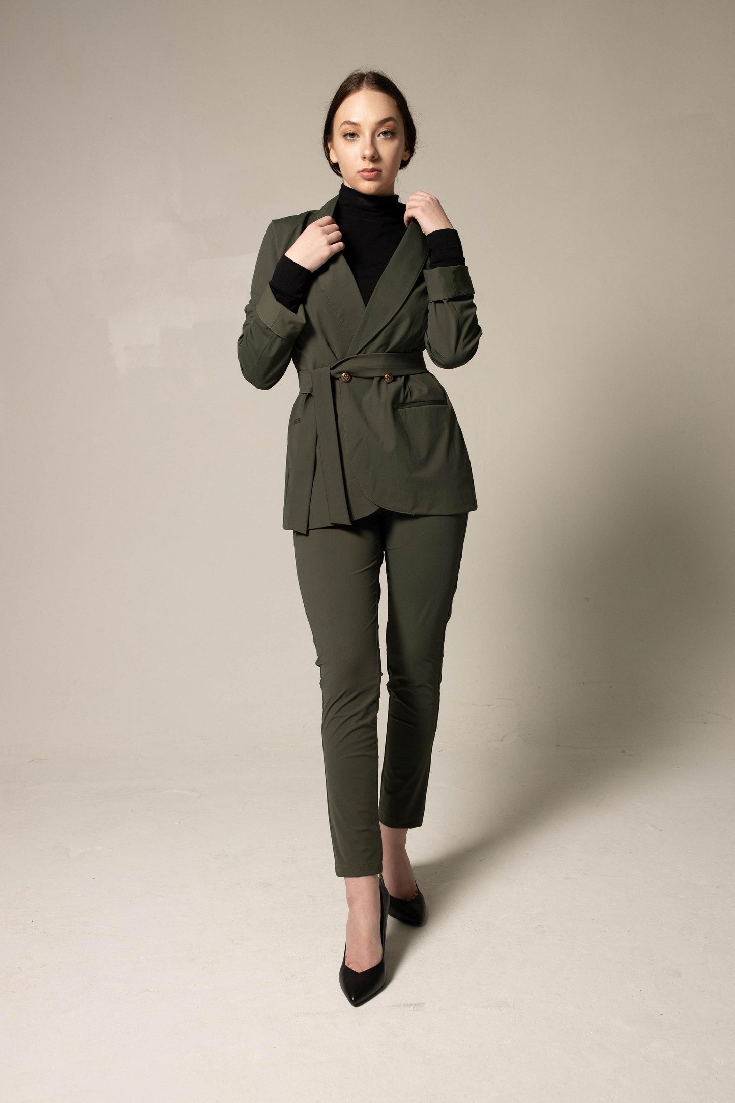 A person wearing a black turtleneck, Le Réussi® Olive Skinny Pants Womens Trousers, and black heels stands against a plain background.