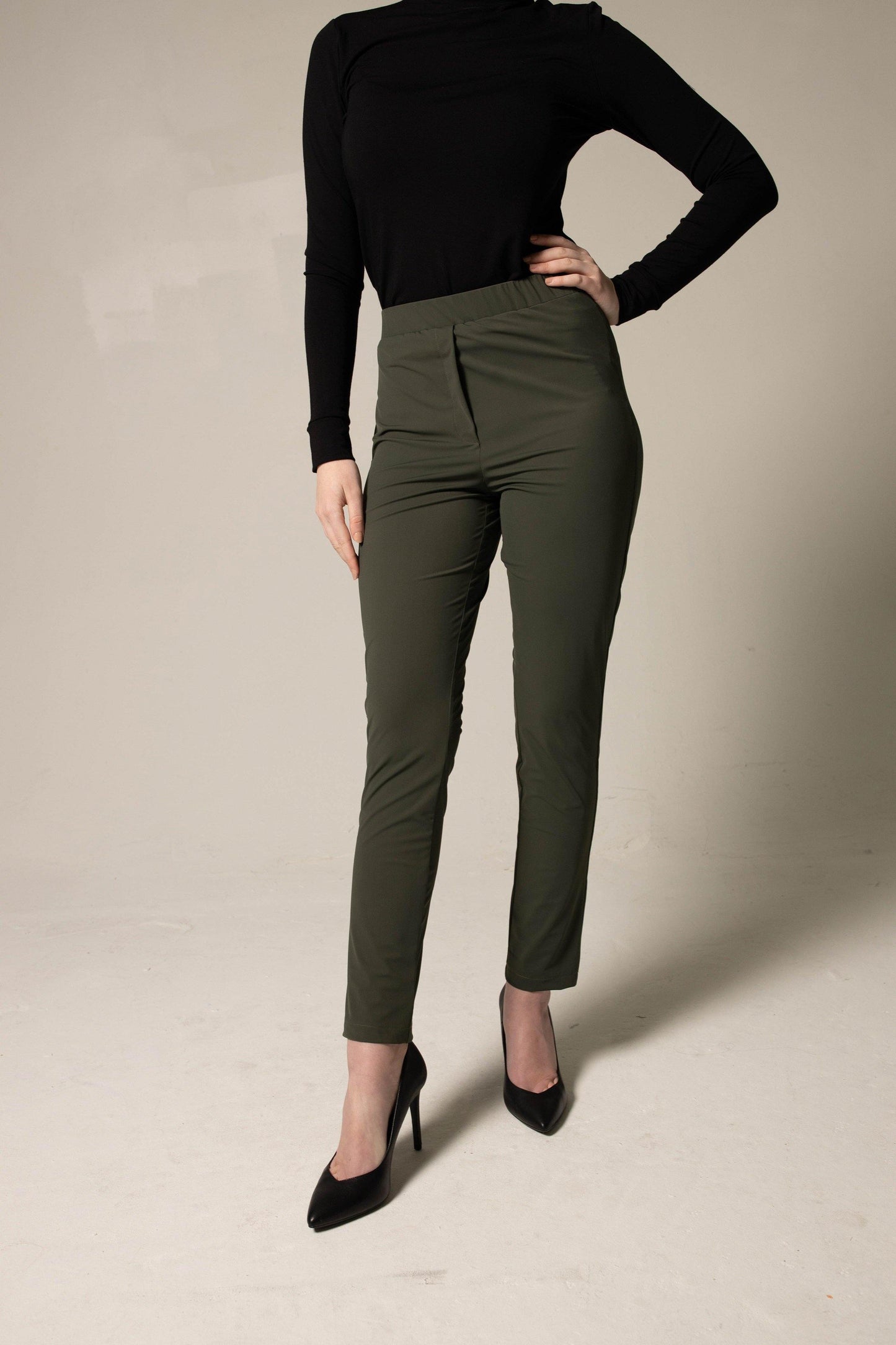A person wearing a black turtleneck, Le Réussi® Olive Skinny Pants Womens Trousers, and black heels stands against a plain background.