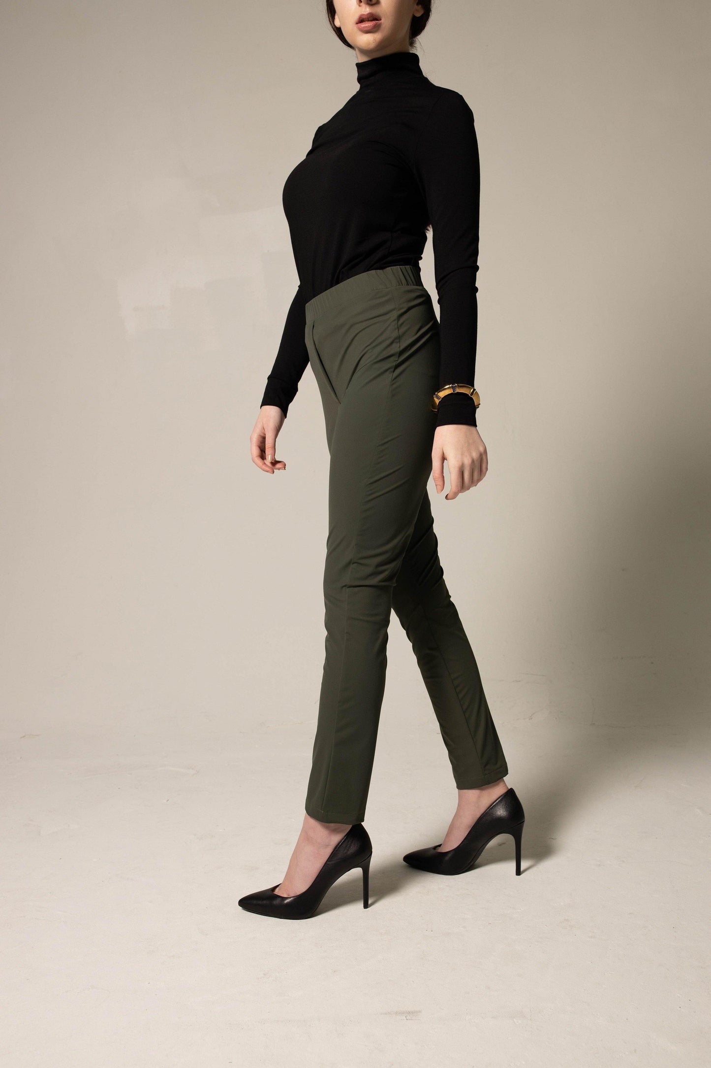 A person wearing a black turtleneck, Le Réussi® Olive Skinny Pants Womens Trousers, and black heels stands against a plain background.