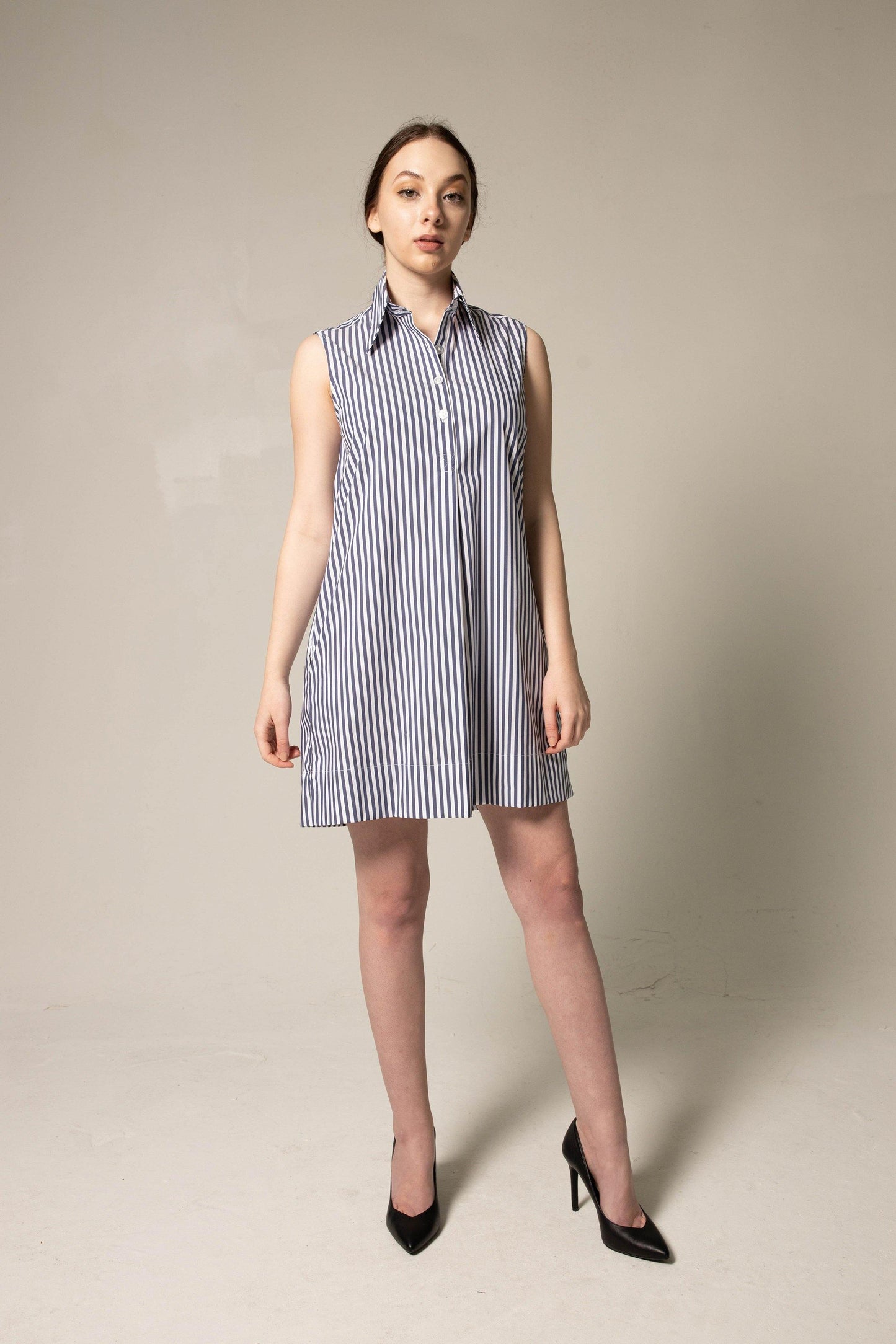 A model showcases the Italian Cotton Blue Stripe Sleeveless Dress by Le Réussi®, paired with black heels against a plain beige background.