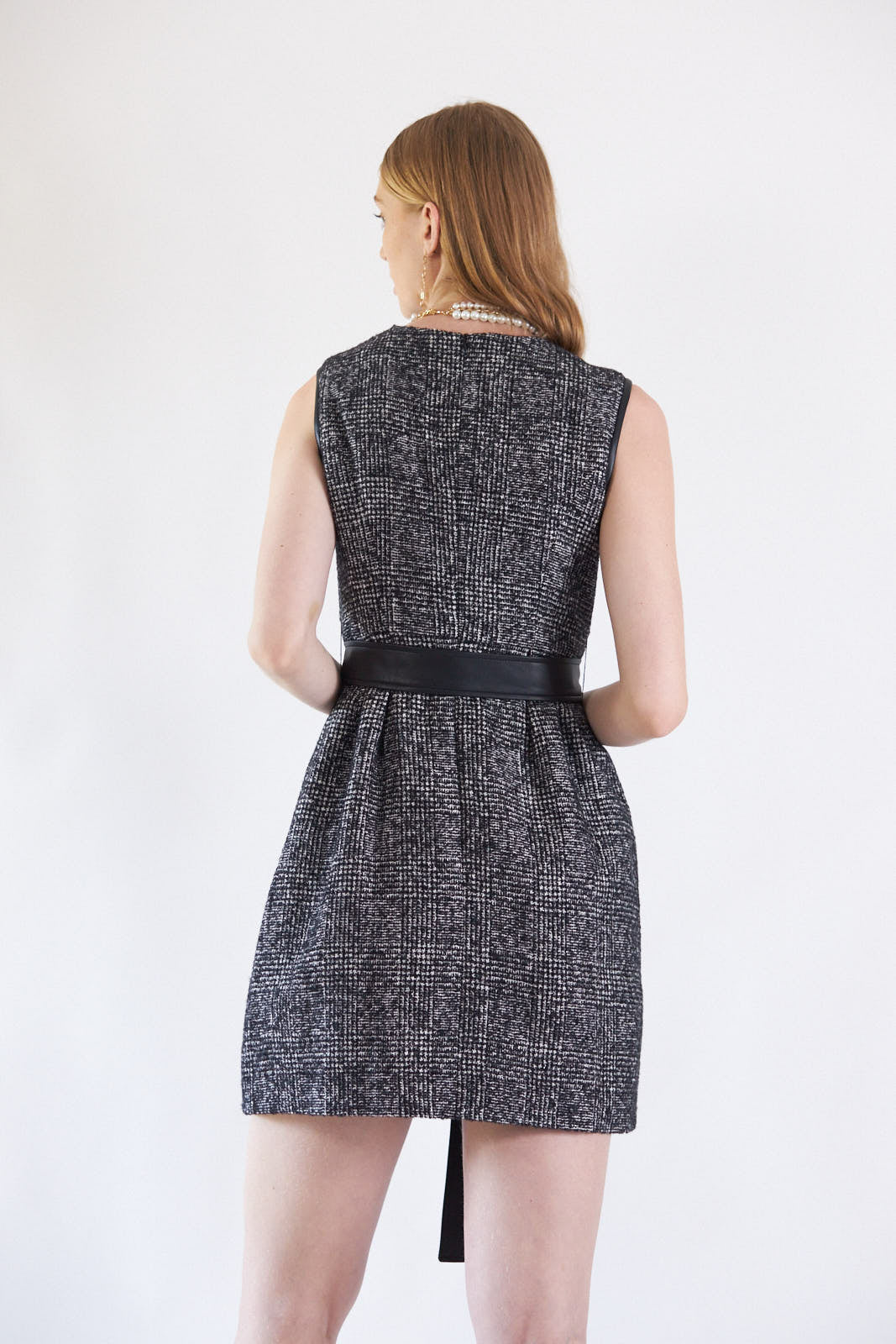 A person standing against a white background wears the Boss Woman Tweed Dress by Le Réussi®, accessorized with layered necklaces, a black belt, and black ankle boots.