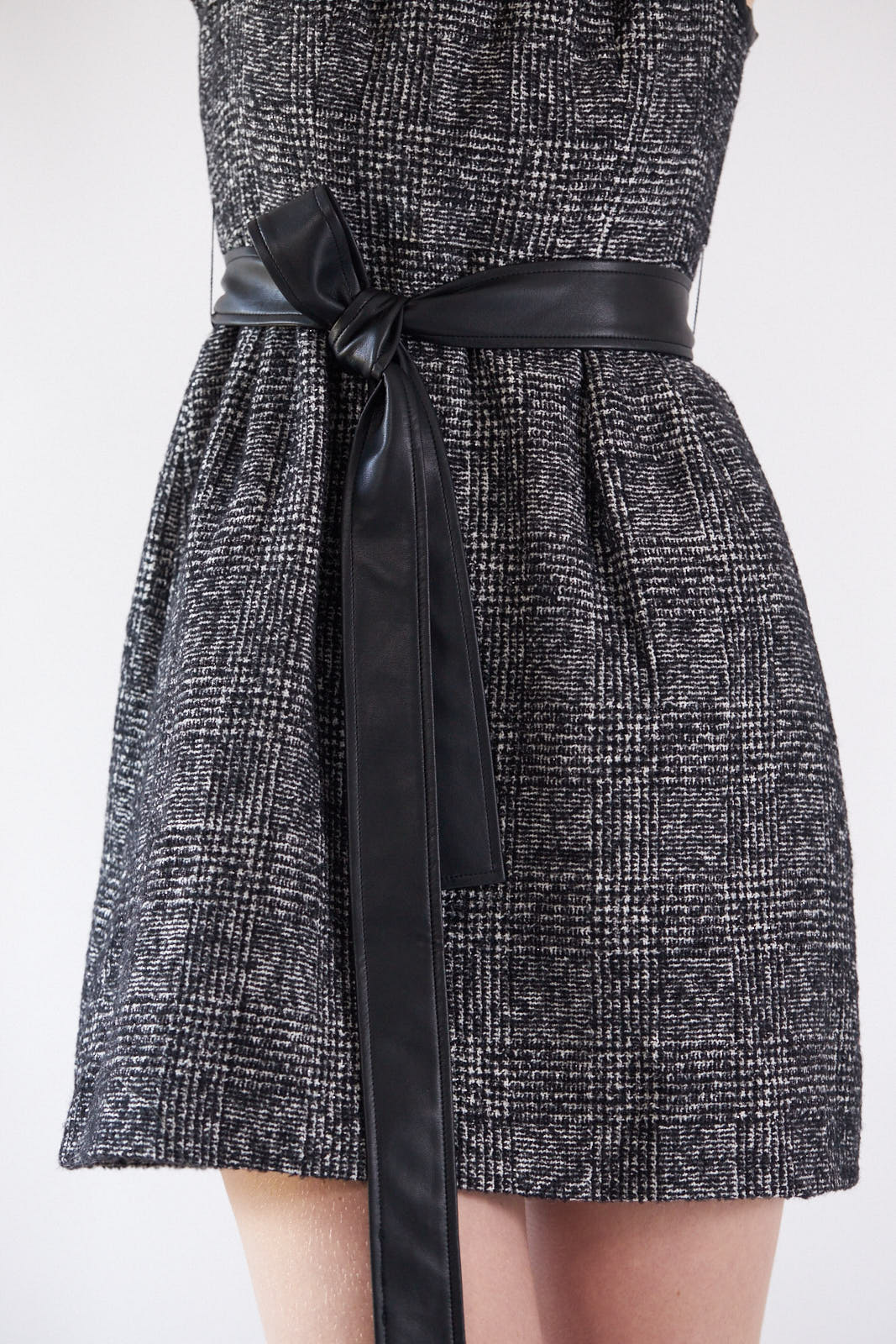 A person standing against a white background wears the Boss Woman Tweed Dress by Le Réussi®, accessorized with layered necklaces, a black belt, and black ankle boots.
