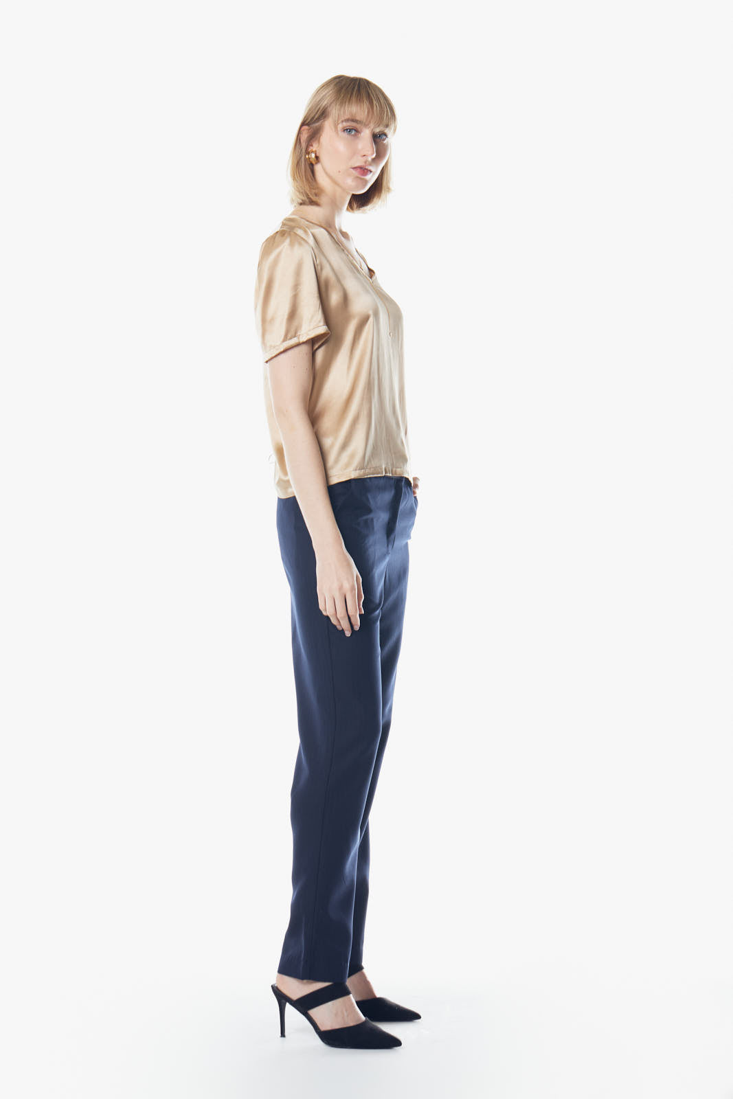 A person wearing the Le Réussi® Champagne V-Neck Blouse and dark pants stands against a white background, hands in pockets.