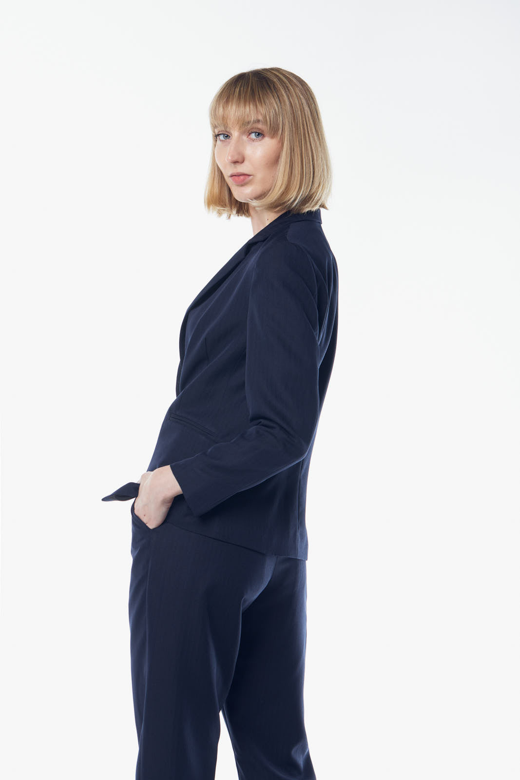 A person in a suit, wearing the Le Réussi® Navy Peak-Lapels Single-Breasted Blazer, stands smiling with one hand on their forehead against a plain background.