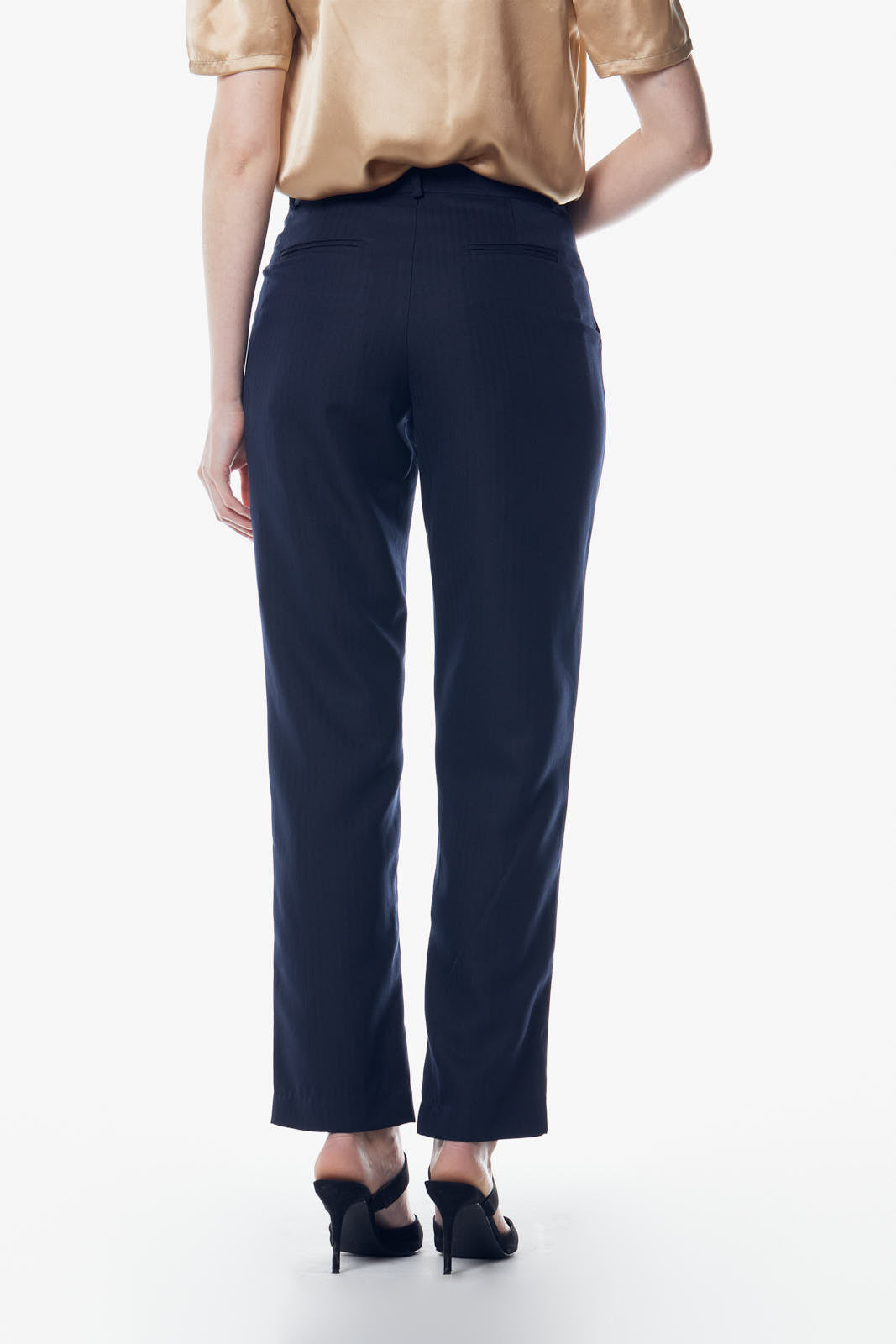 Person in Italian Wool Skinny Pants by Le Réussi®, a dark suit, heels, and a scarf stands against a plain background.