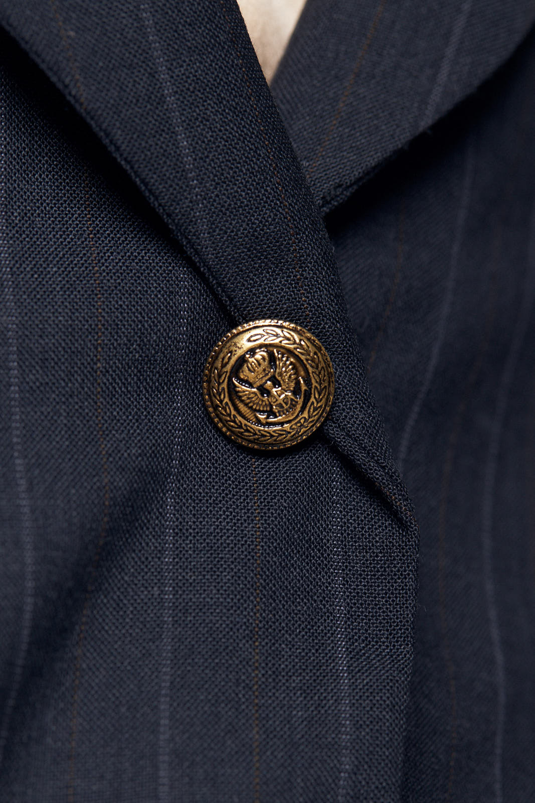 A person with short blond hair poses confidently in a beige top, skirt, and the Tailor Wool Dark Grey Blazer by Le Réussi® against a white background.