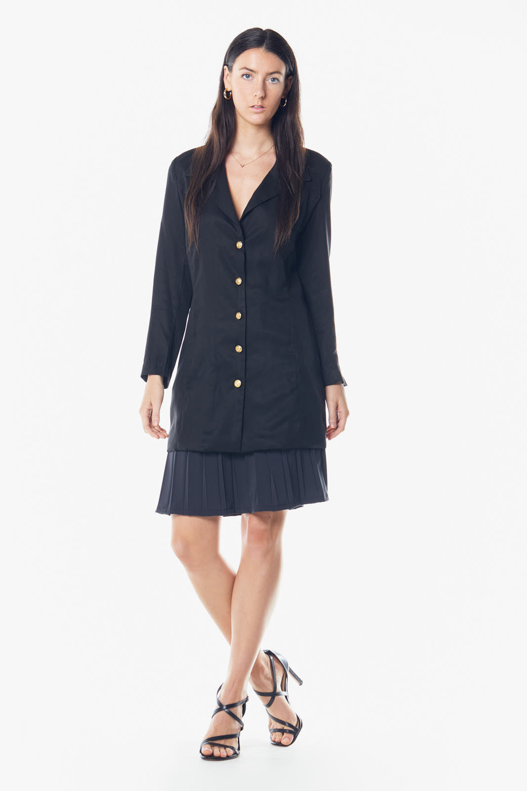 A woman in a black Linen Long Jacket by Le Réussi® stands against a white background, paired with black strappy heels.