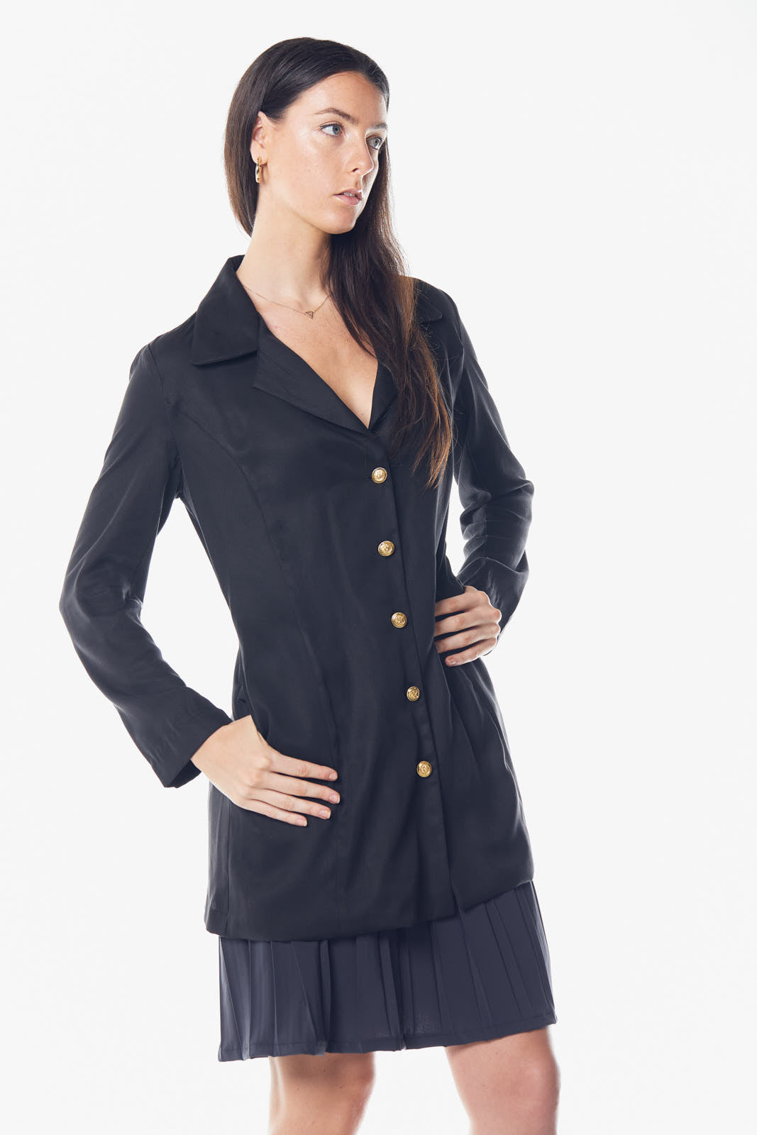 A woman in a black Linen Long Jacket by Le Réussi® stands against a white background, paired with black strappy heels.