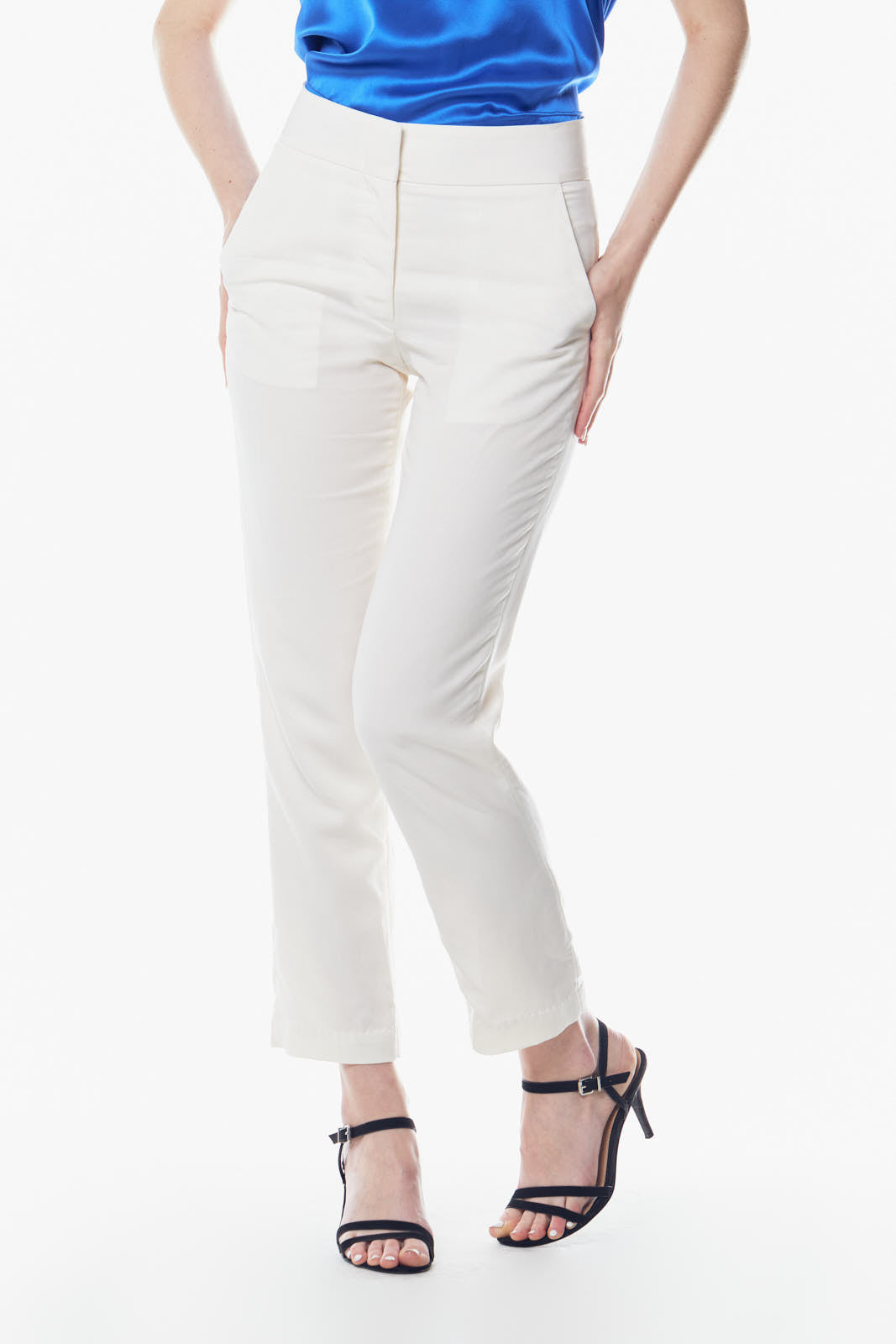 A person is wearing Le Réussi® White Skinny Pants and black strappy sandals, standing against a white background. Their blue top is partially visible.