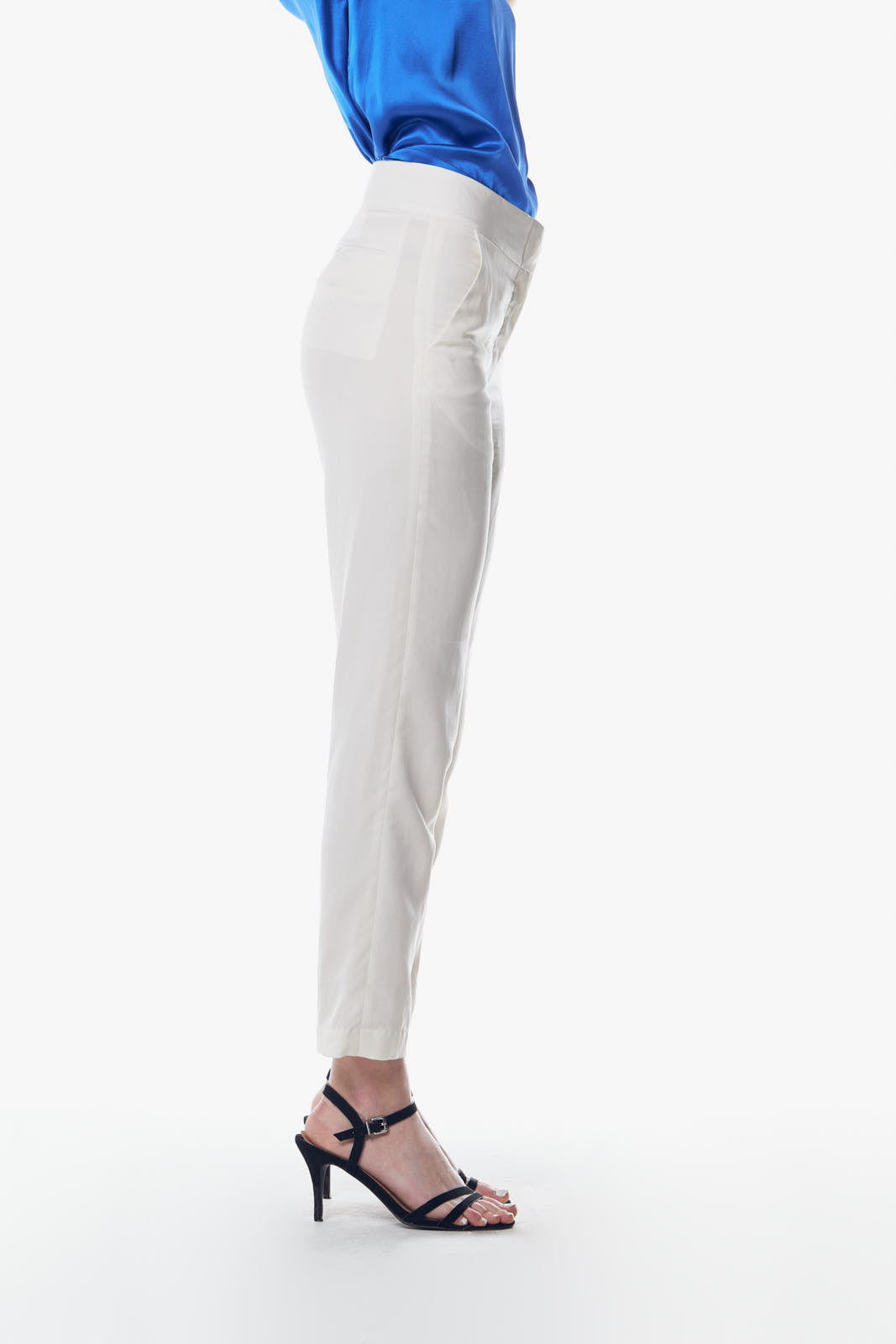 A person is wearing Le Réussi® White Skinny Pants and black strappy sandals, standing against a white background. Their blue top is partially visible.