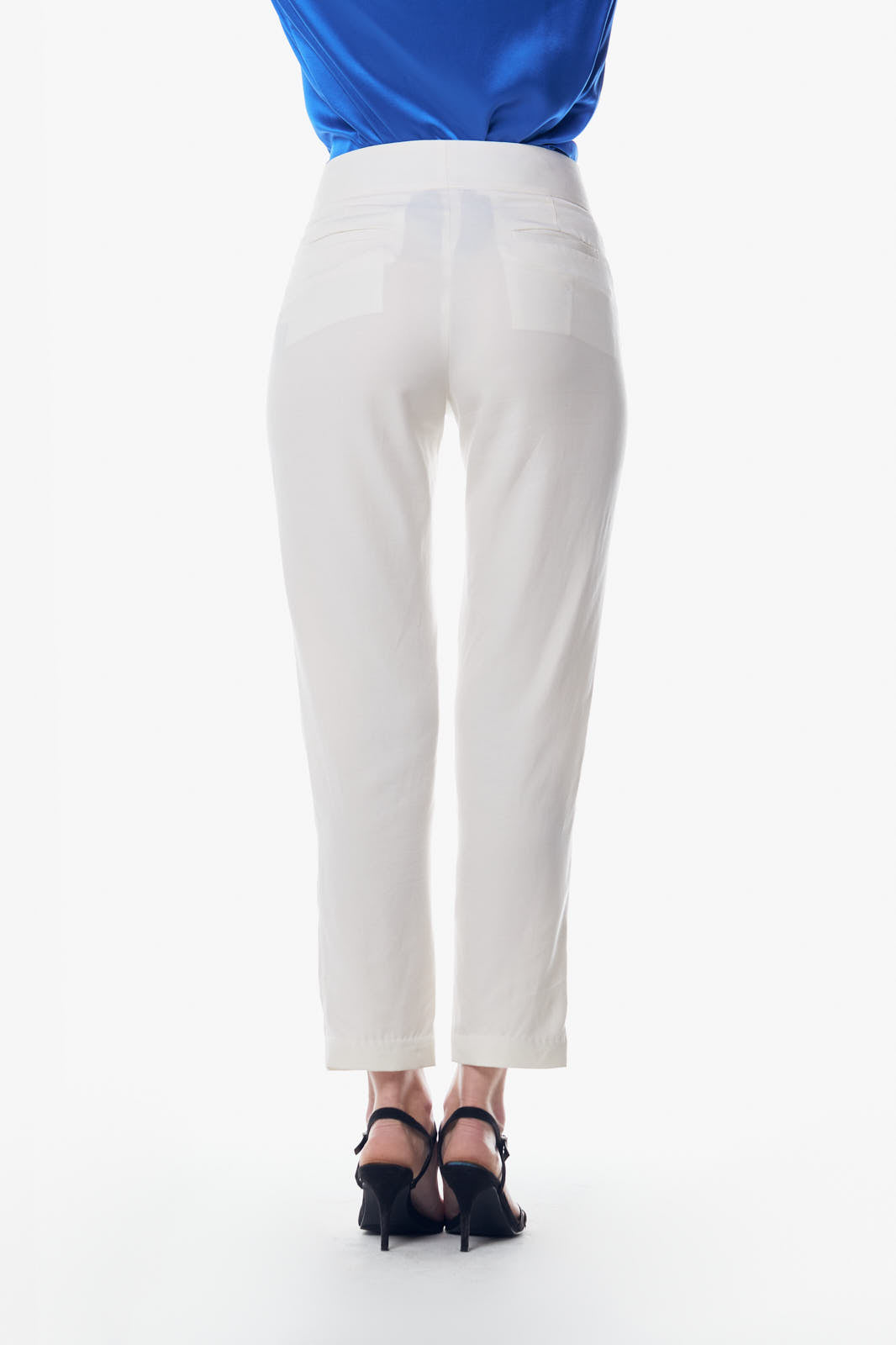 A person is wearing Le Réussi® White Skinny Pants and black strappy sandals, standing against a white background. Their blue top is partially visible.