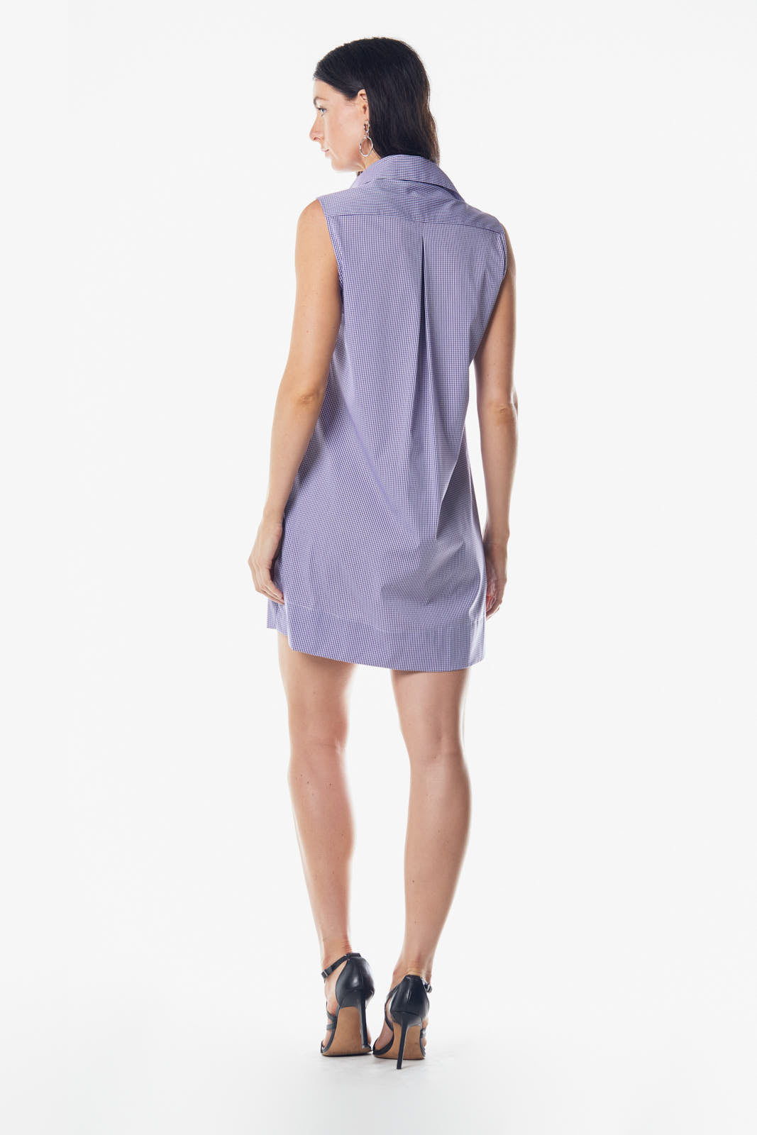 A woman exudes confidence in a Le Réussi® Italian Cotton Sleeveless Dress in Purple, featuring a collar and front pleat. She pairs the dress with high-heeled sandals, her long hair cascading freely.