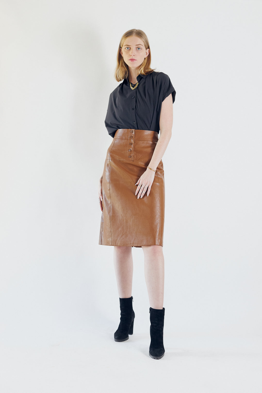 A person wearing a black top, Le Réussi® Power Woman- Dark Hazel Leather Skirt, and black high-heeled boots poses against a plain background.