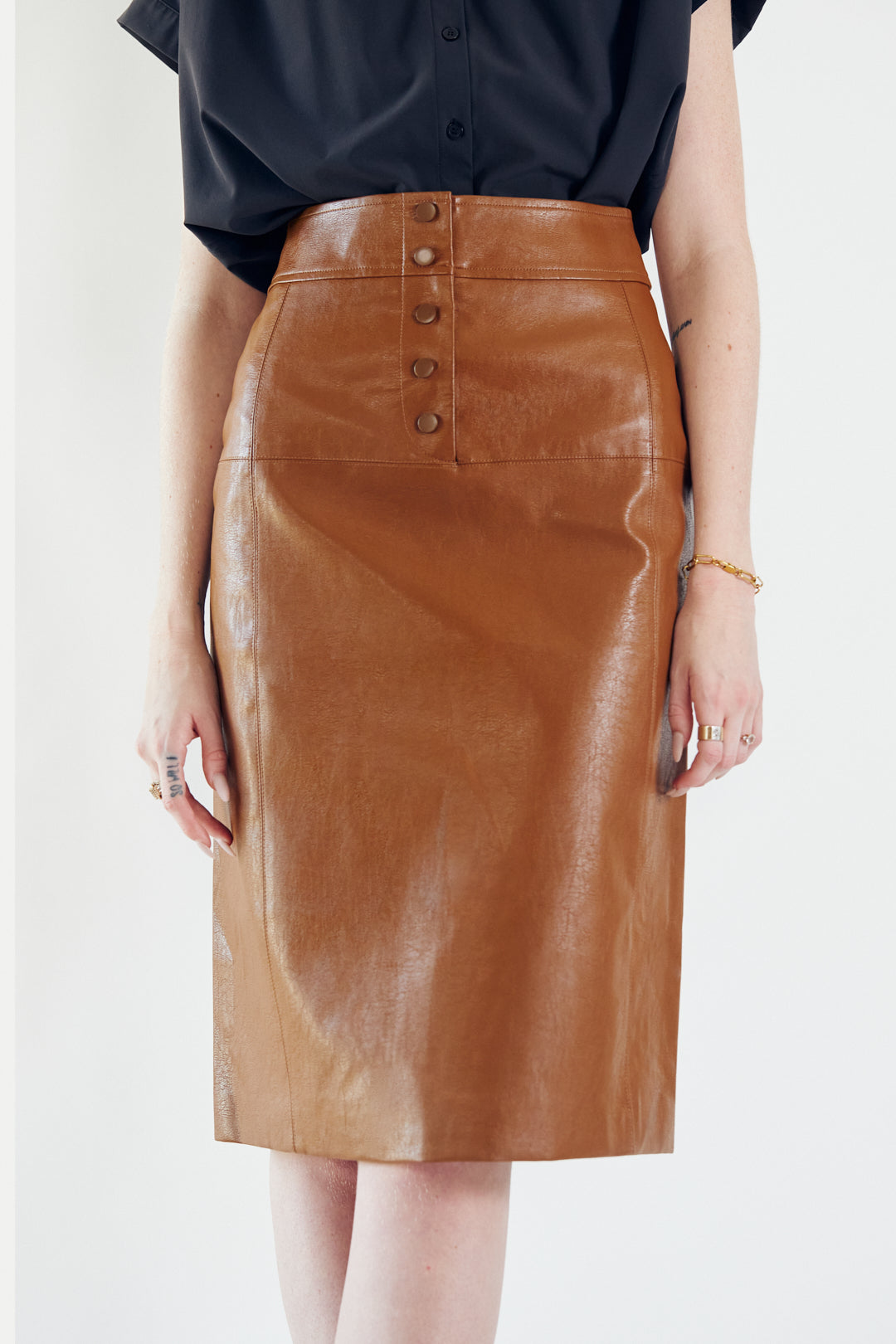 A person wearing a black top, Le Réussi® Power Woman- Dark Hazel Leather Skirt, and black high-heeled boots poses against a plain background.